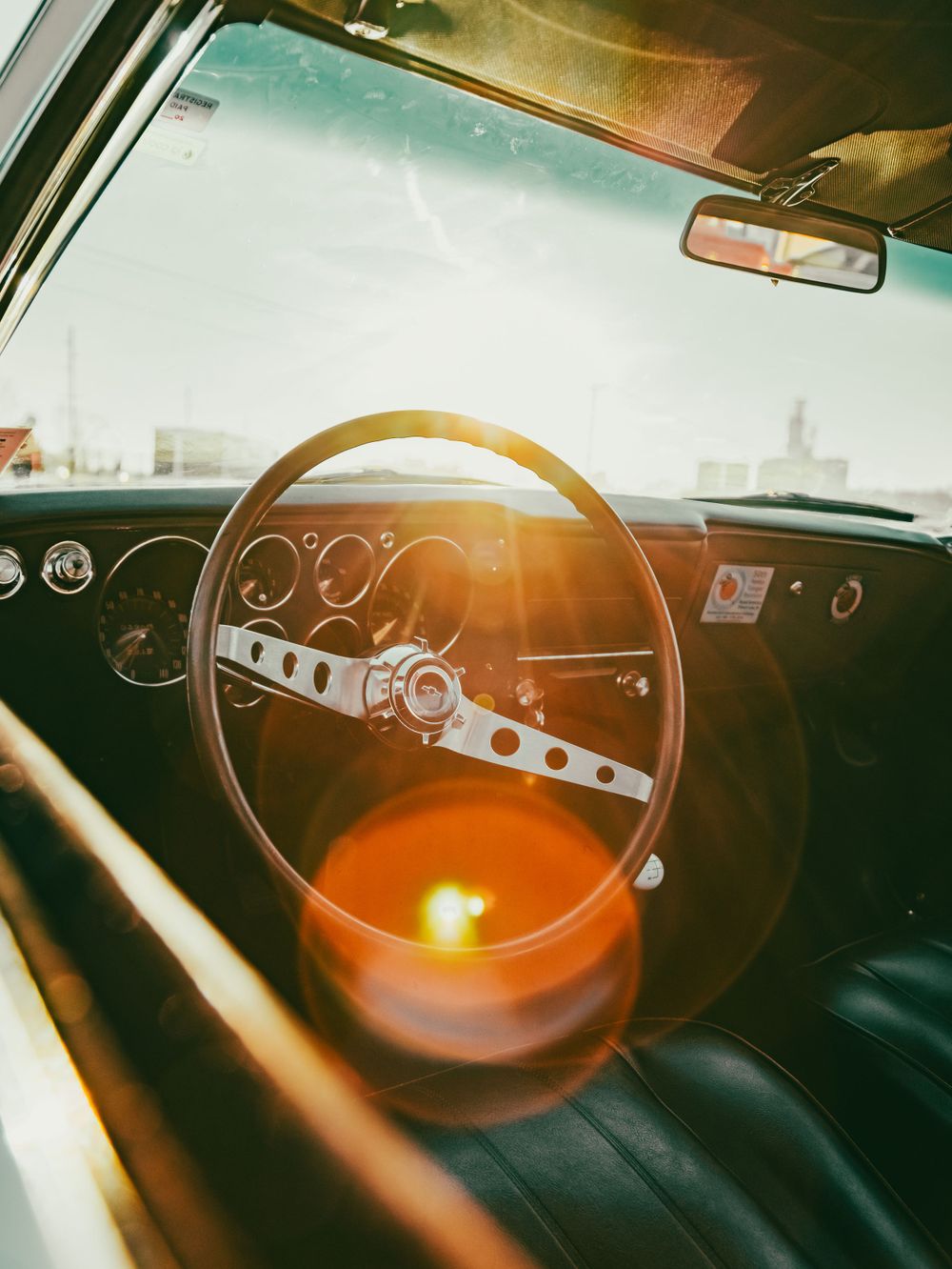 Vintage car interior showing wooden steering wheel and dashboard gauges bathed in warm sunlight.