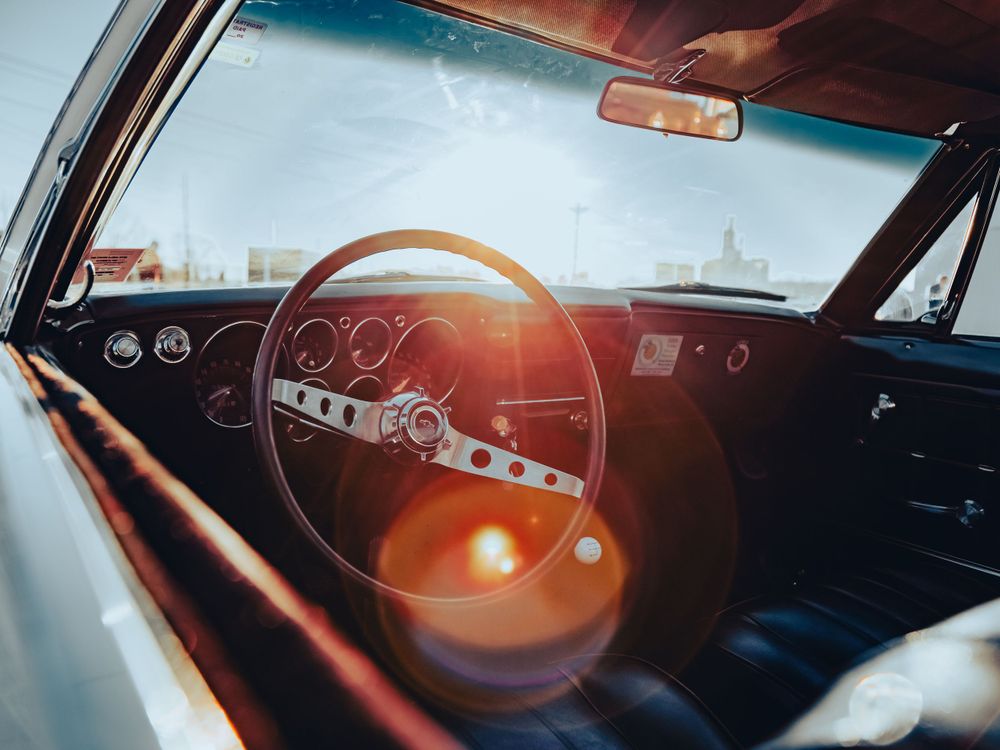 Classic car dashboard and steering wheel photographed through windshield with sun flare.
