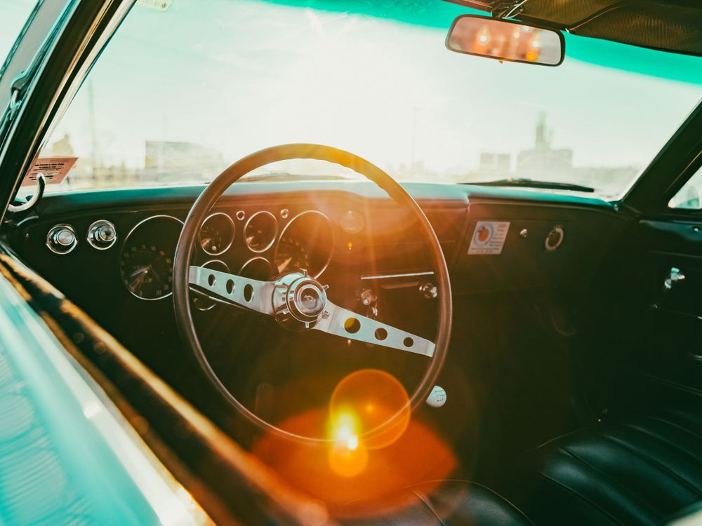 Retro car interior with vintage steering wheel and instrument panel in teal-tinted lighting.