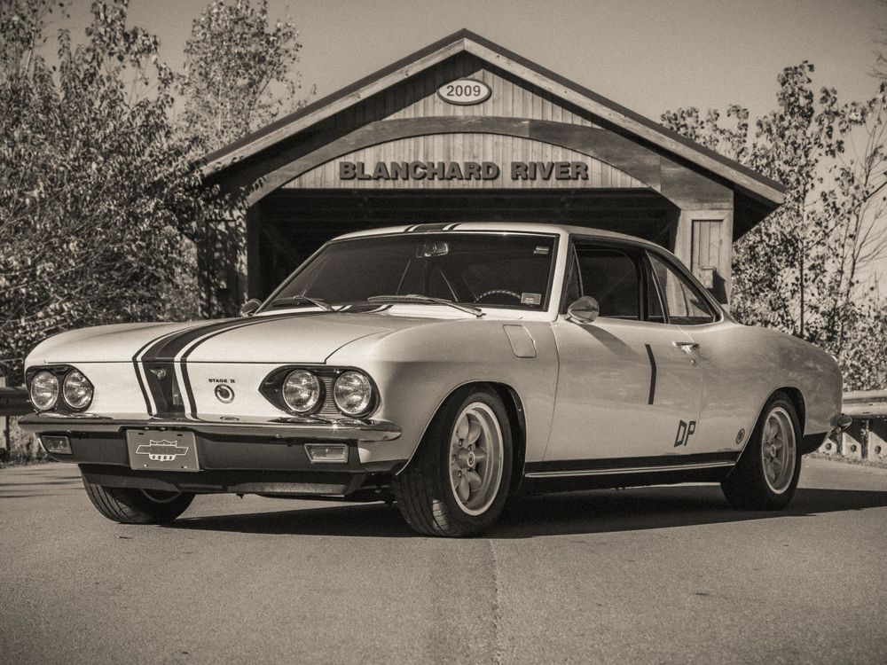 Monochrome image of a restored classic car with racing stripes at Blanchard River bridge.