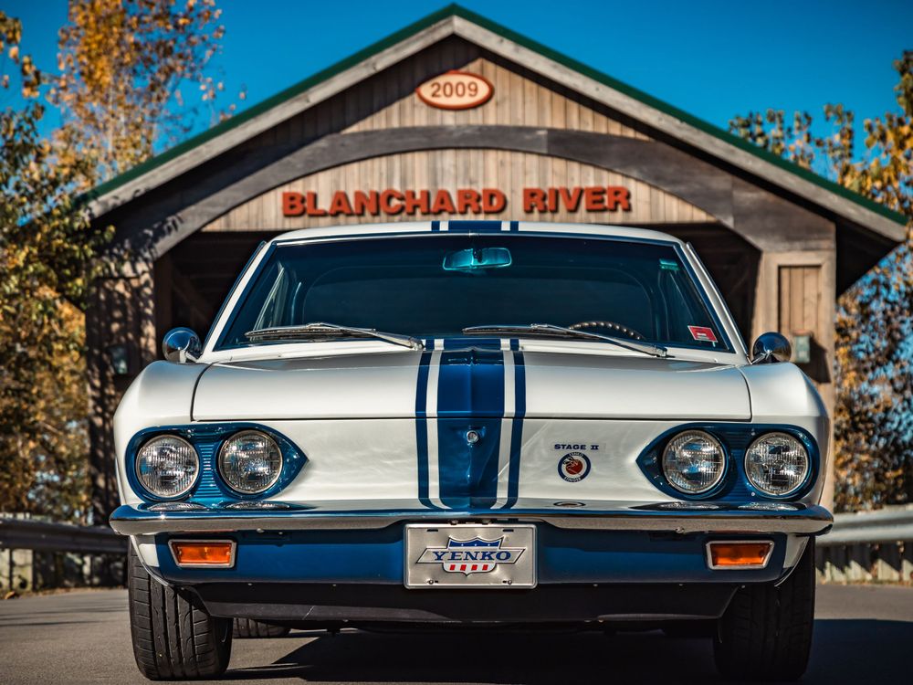Front view of classic white sports car with blue racing stripe at covered bridge entrance.