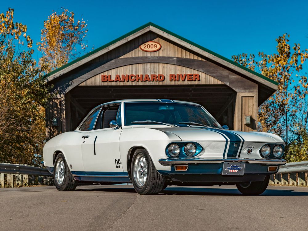 White Yenko Stinger Corvair with distinctive blue stripes captured at rustic covered bridge entrance.