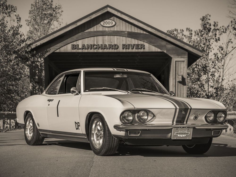 Black and white photo of a vintage Corvair coupe parked in front of Blanchard River covered bridge.