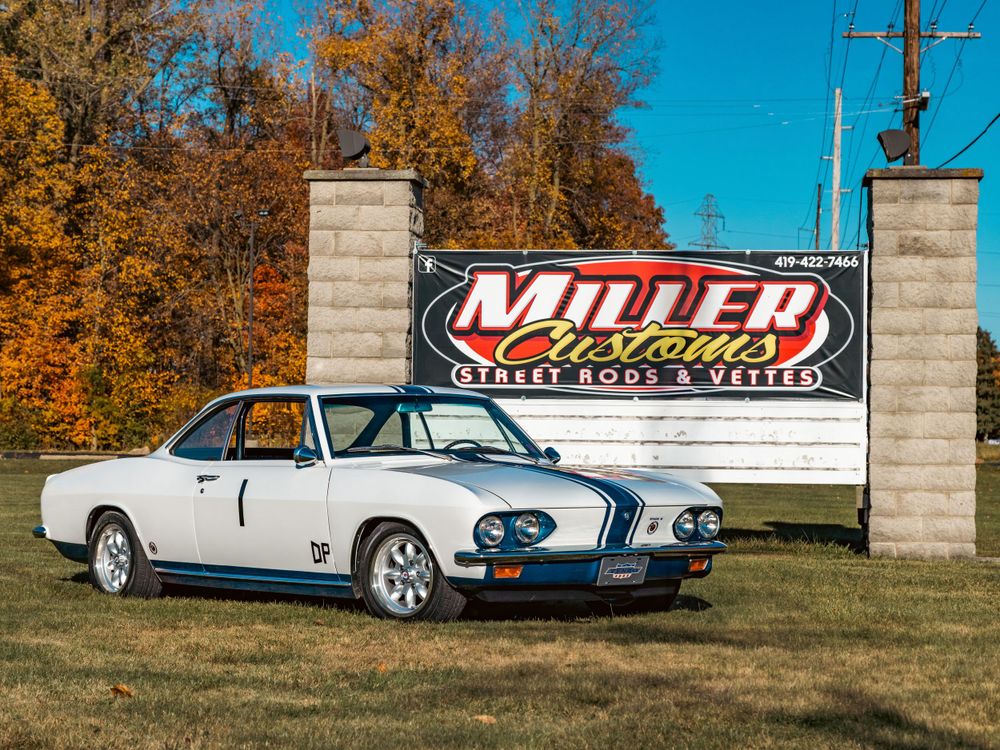 Classic white sports car displayed in front of Miller Motorsports sign during autumn.