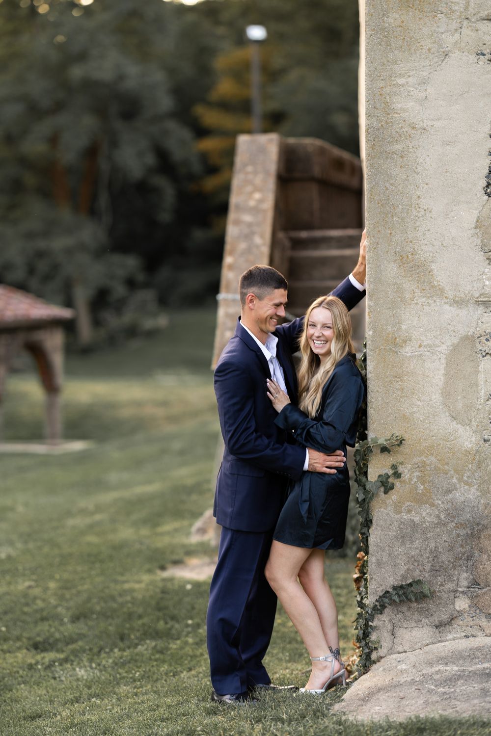 Couple sharing intimate moment against stone pillar in garden setting.