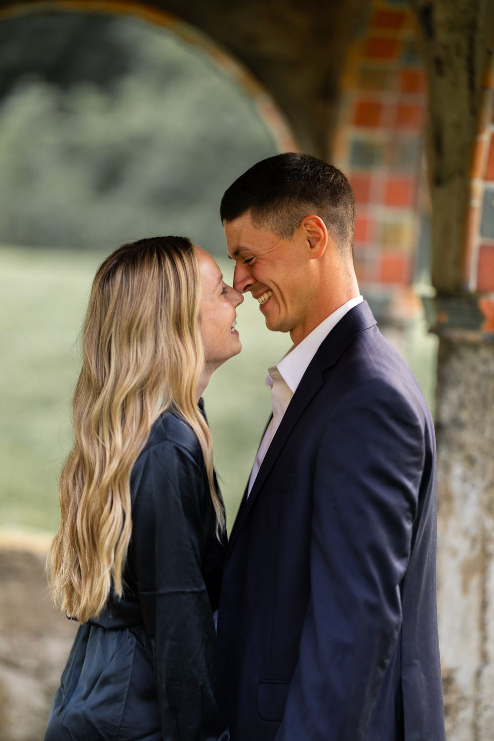 Intimate close-up moment between couple under brick archway.