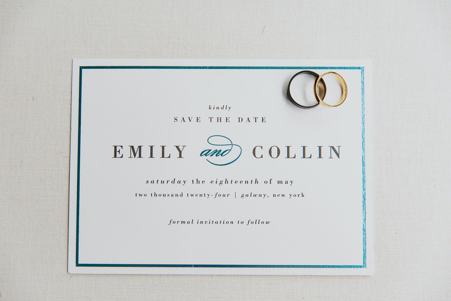 Wedding invitation with two gold wedding rings on top of a simple white and blue card design.