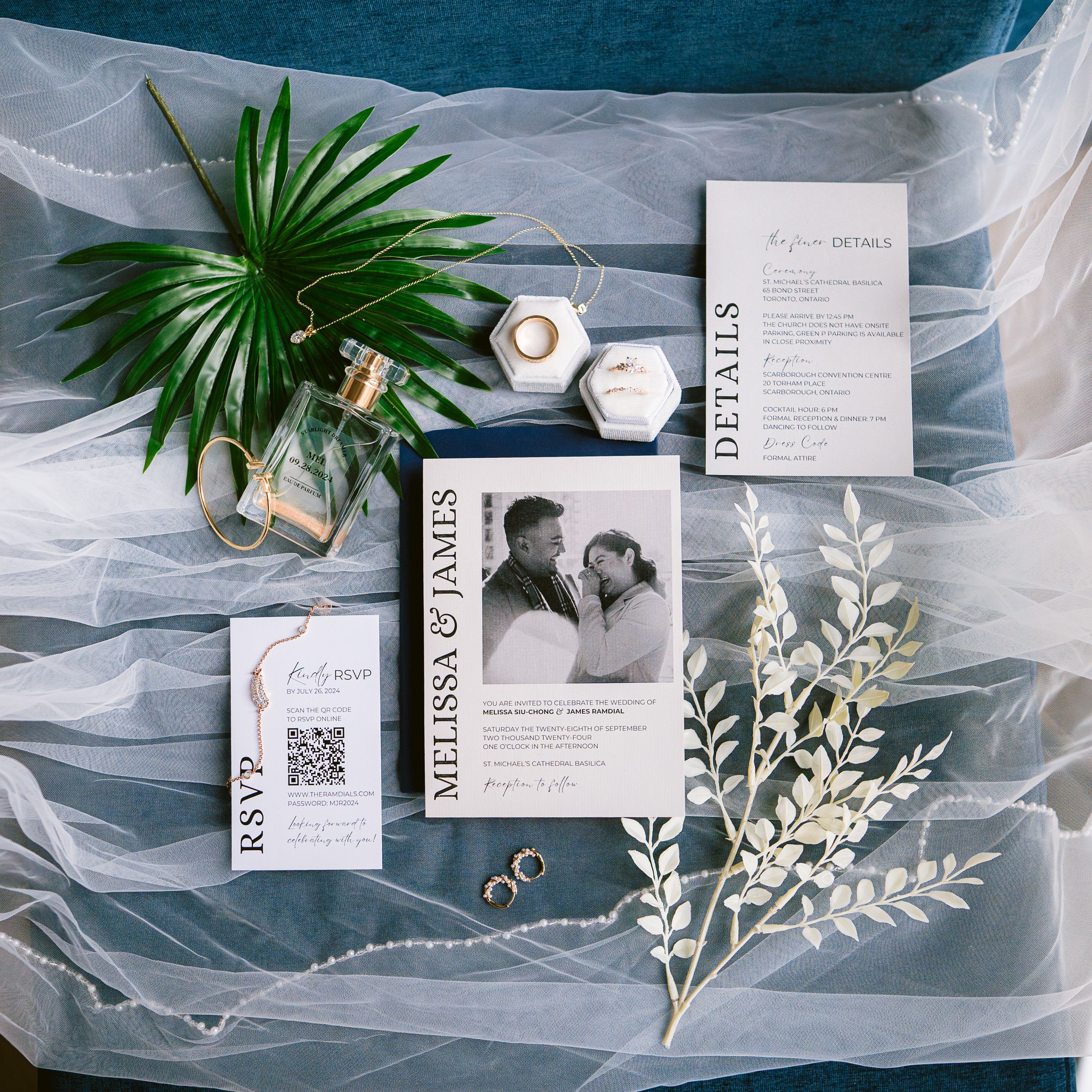 Wedding invitation suite with rings, candles, and greenery styled on blue tulle fabric.