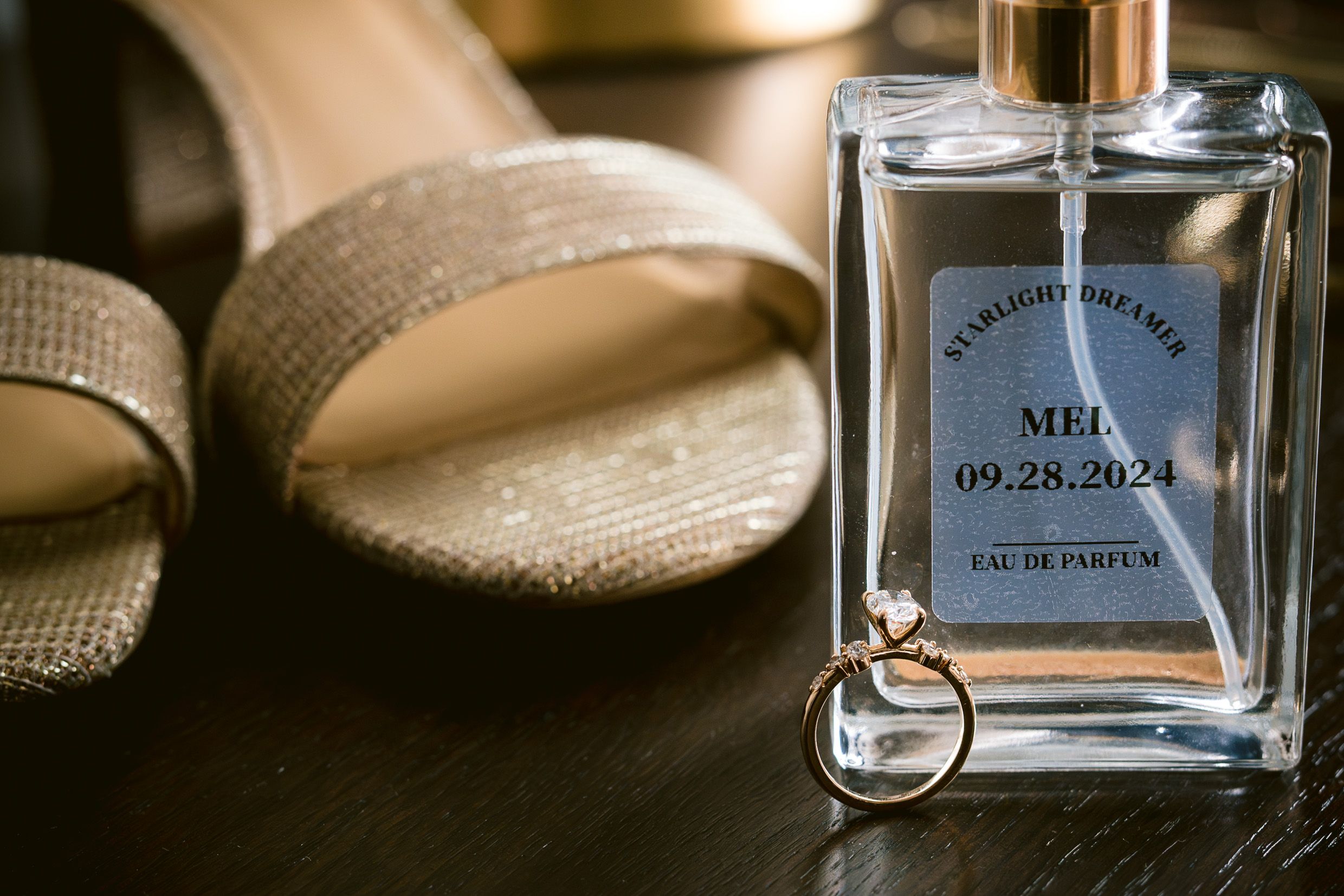 A perfume bottle and ring displayed next to beige slippers in soft lighting.