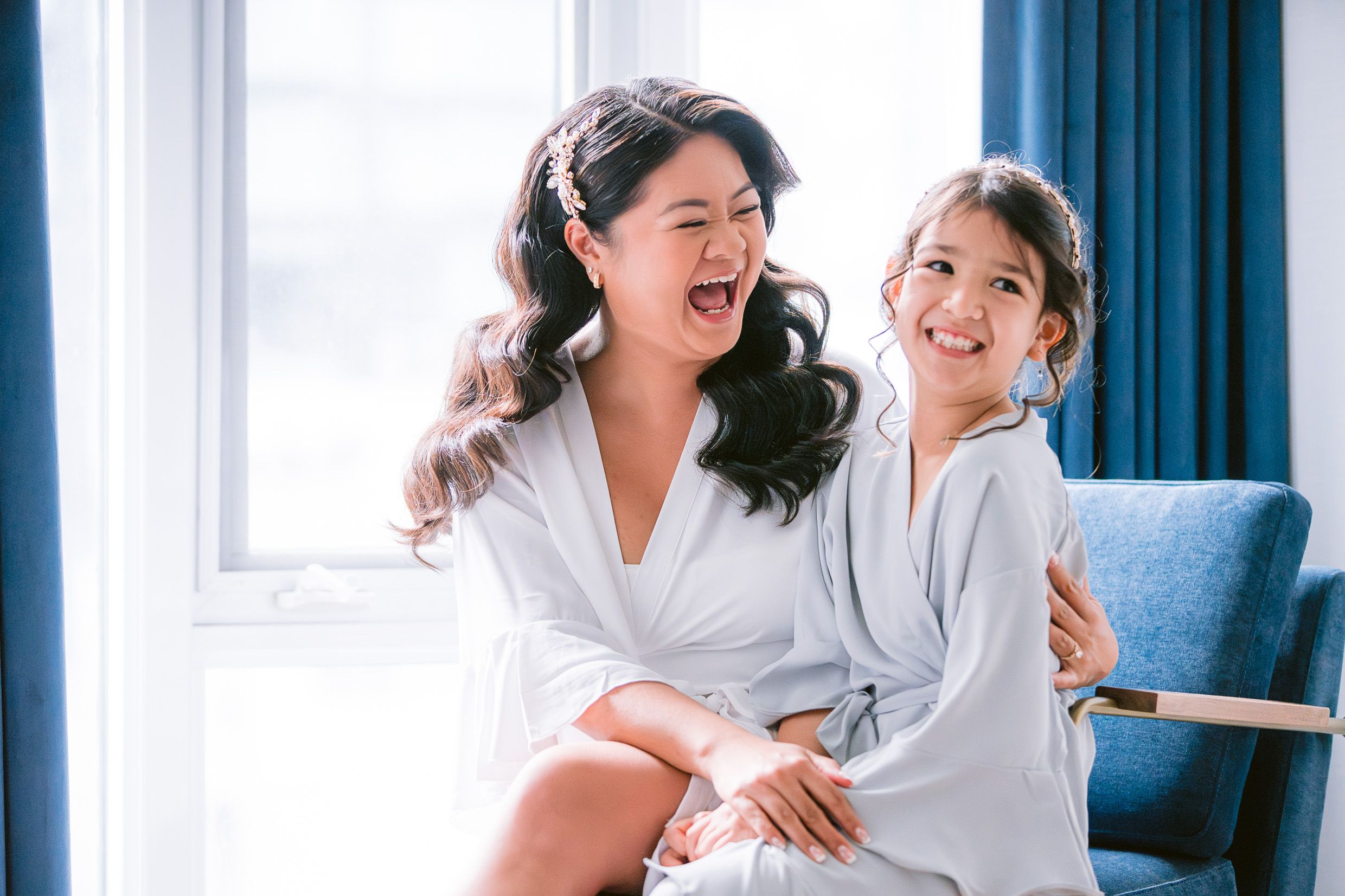 Two people wearing white robes share a joyful moment together while sitting on a blue couch.
