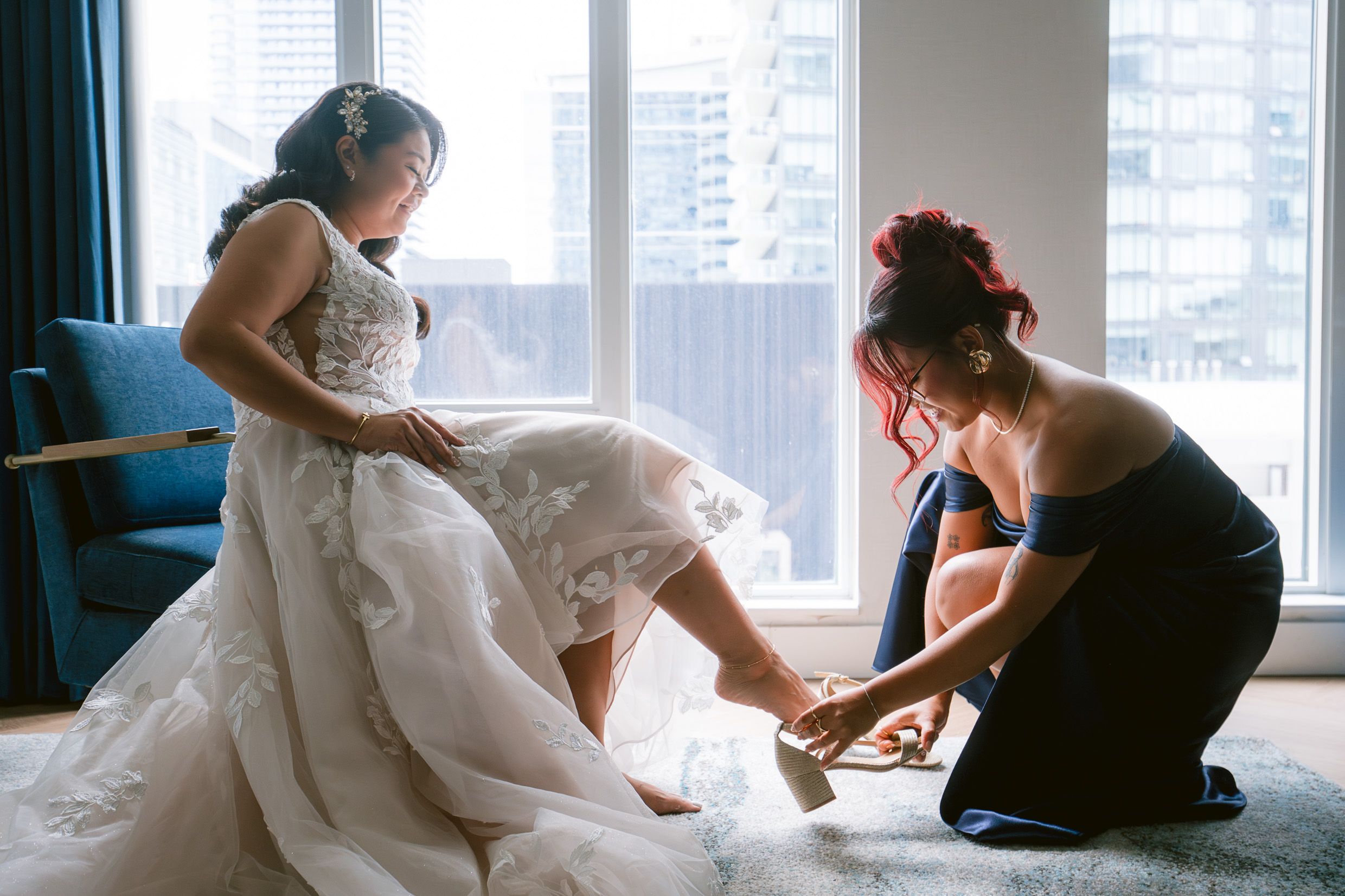Wedding preparation scene showing final dress adjustments in a bright city apartment.