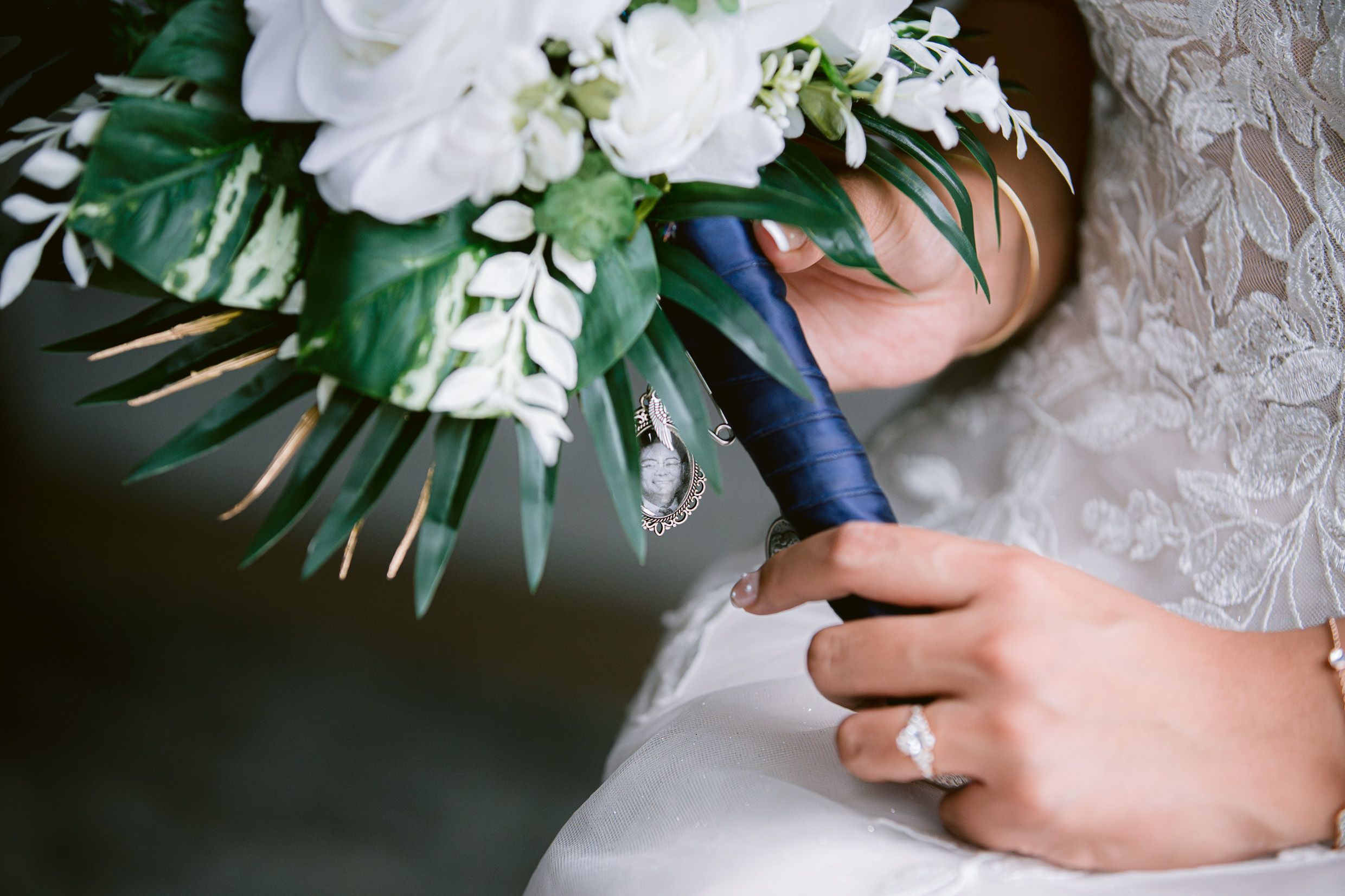 Close-up of hands holding a white and green wedding bouquet with navy blue ribbon accent.