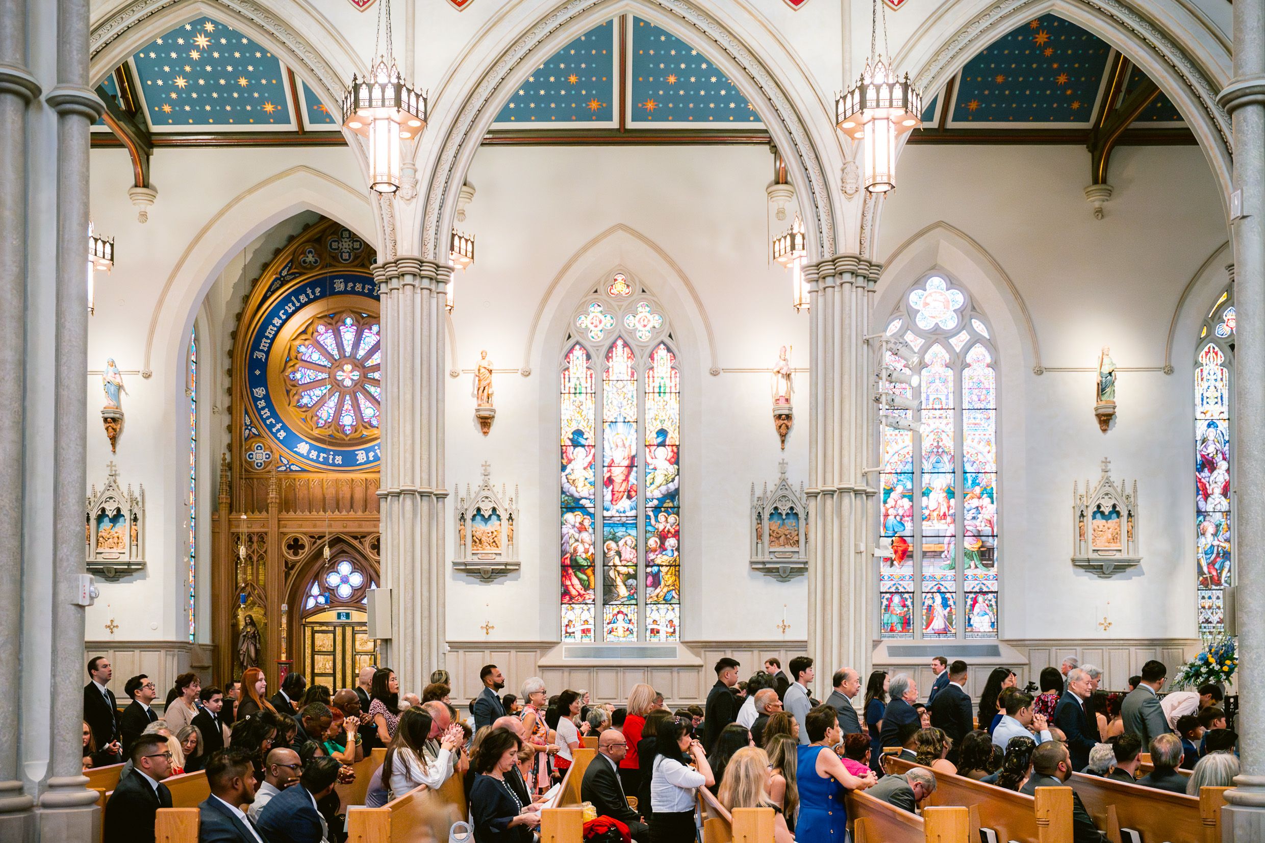 Church interior with arched stained glass windows and guests seated for a wedding ceremony.