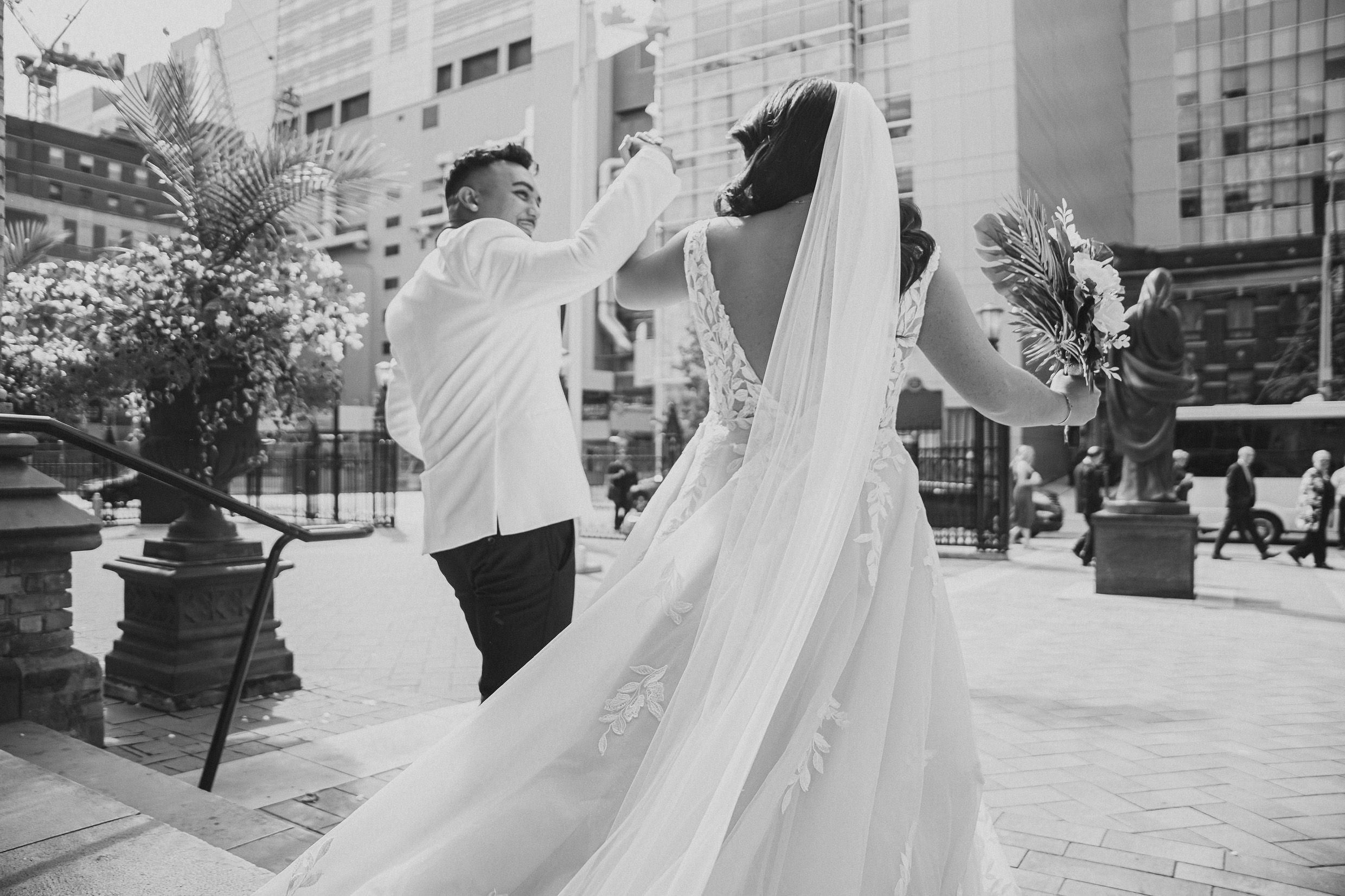 Black and white photo of couple dancing outdoors while bride's veil flows in the wind.