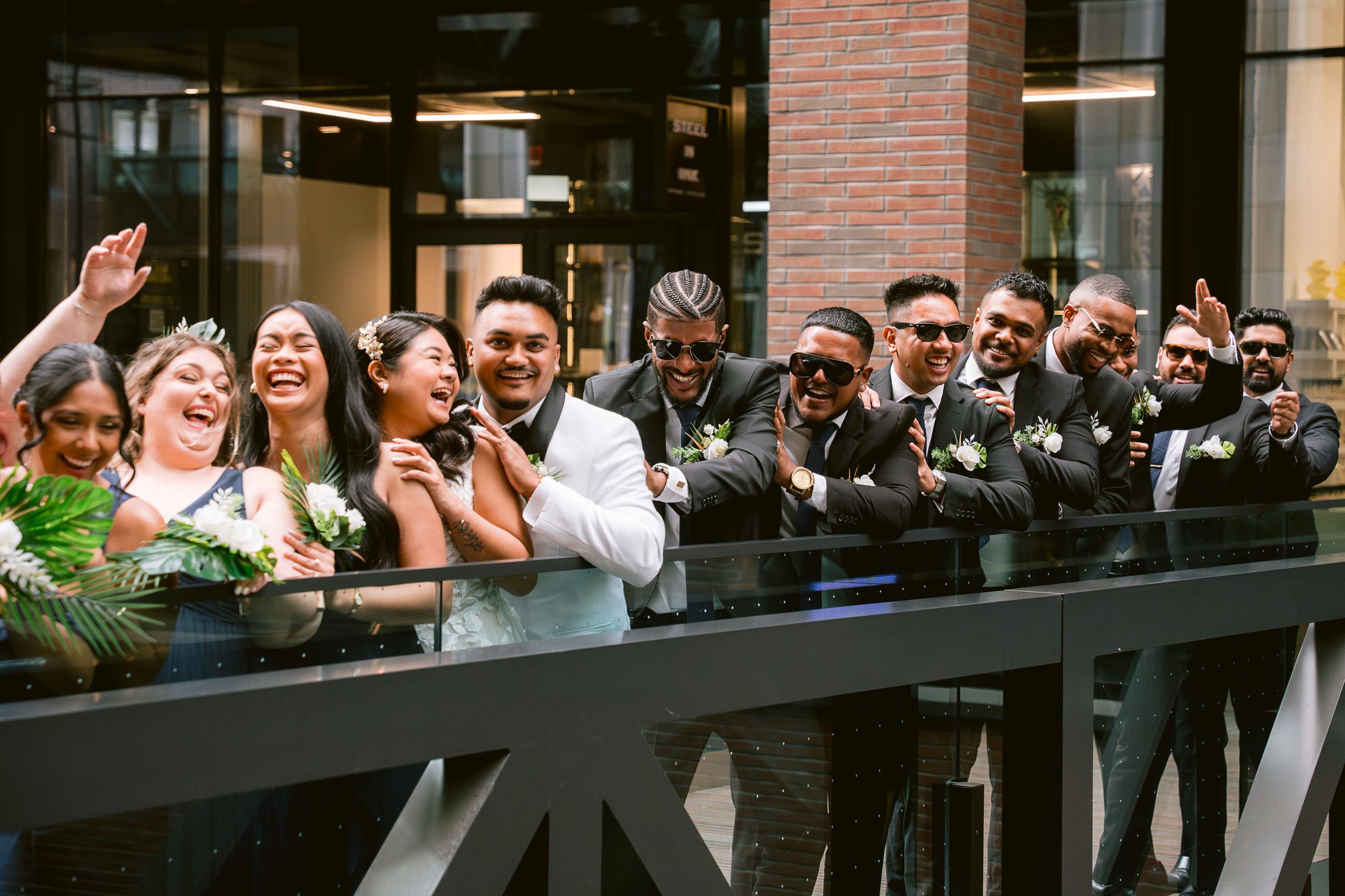 Wedding party laughing together while leaning on a black railing during a joyful celebration.