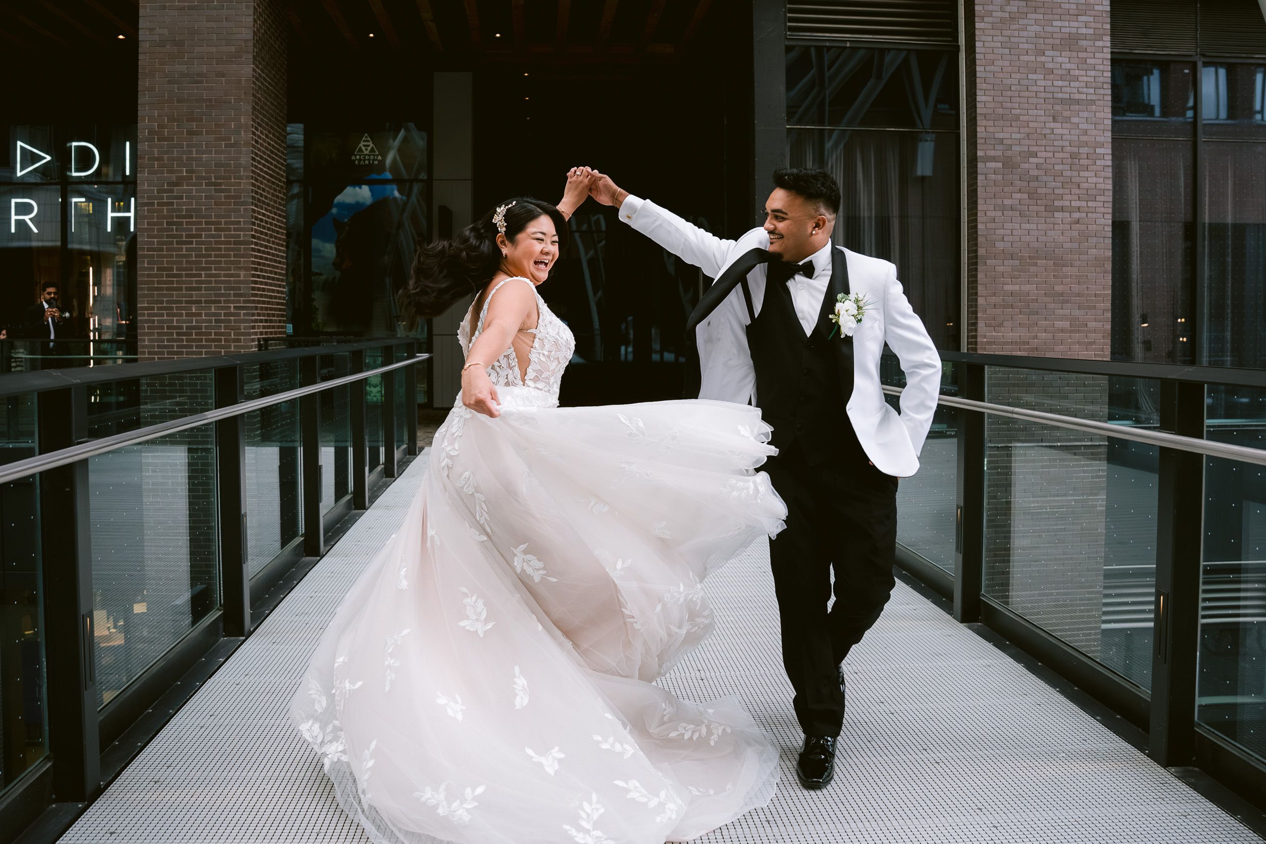 A newlywed couple dances joyfully on an urban walkway as the bride's white lace gown twirls elegantly.