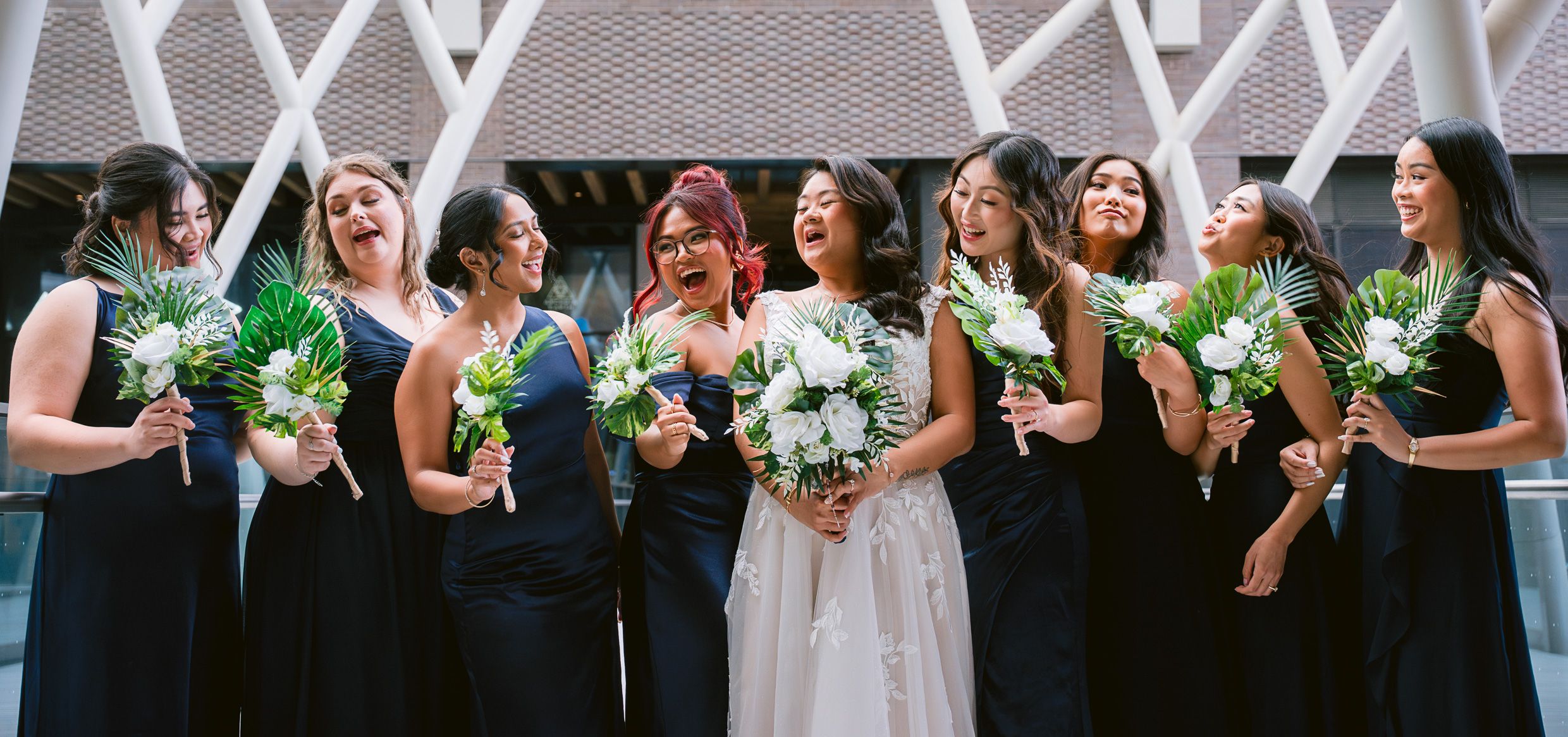 Bridesmaids in navy dresses holding green and white bouquets pose outdoors.