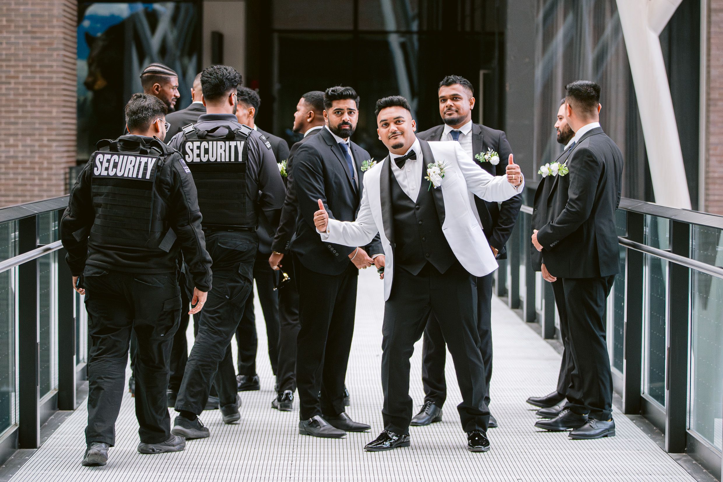 Wedding party and security staff gathered in modern building hallway.