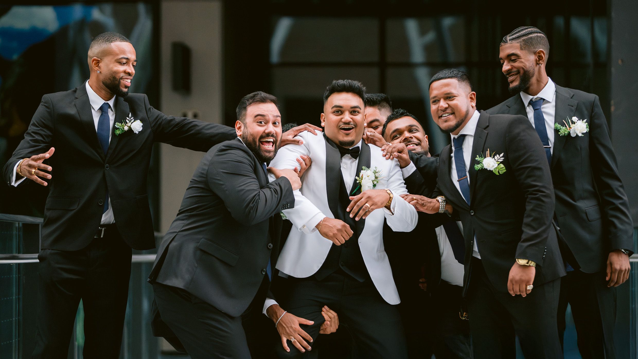 Groomsmen in dark suits and white tuxedo jacket celebrate with joyful expressions.