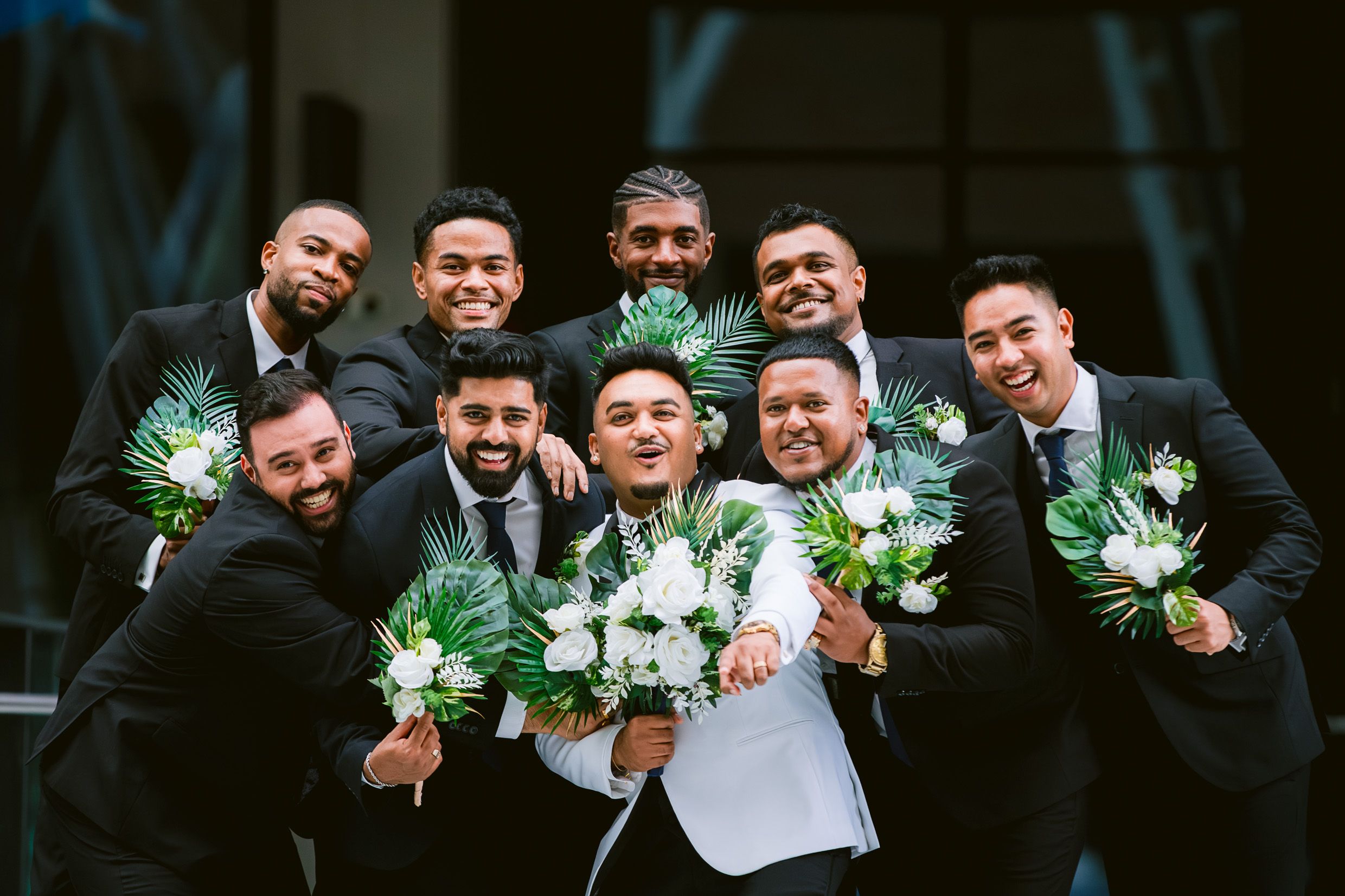 Groomsmen in black suits with boutonnieres pose together for a celebratory photo.