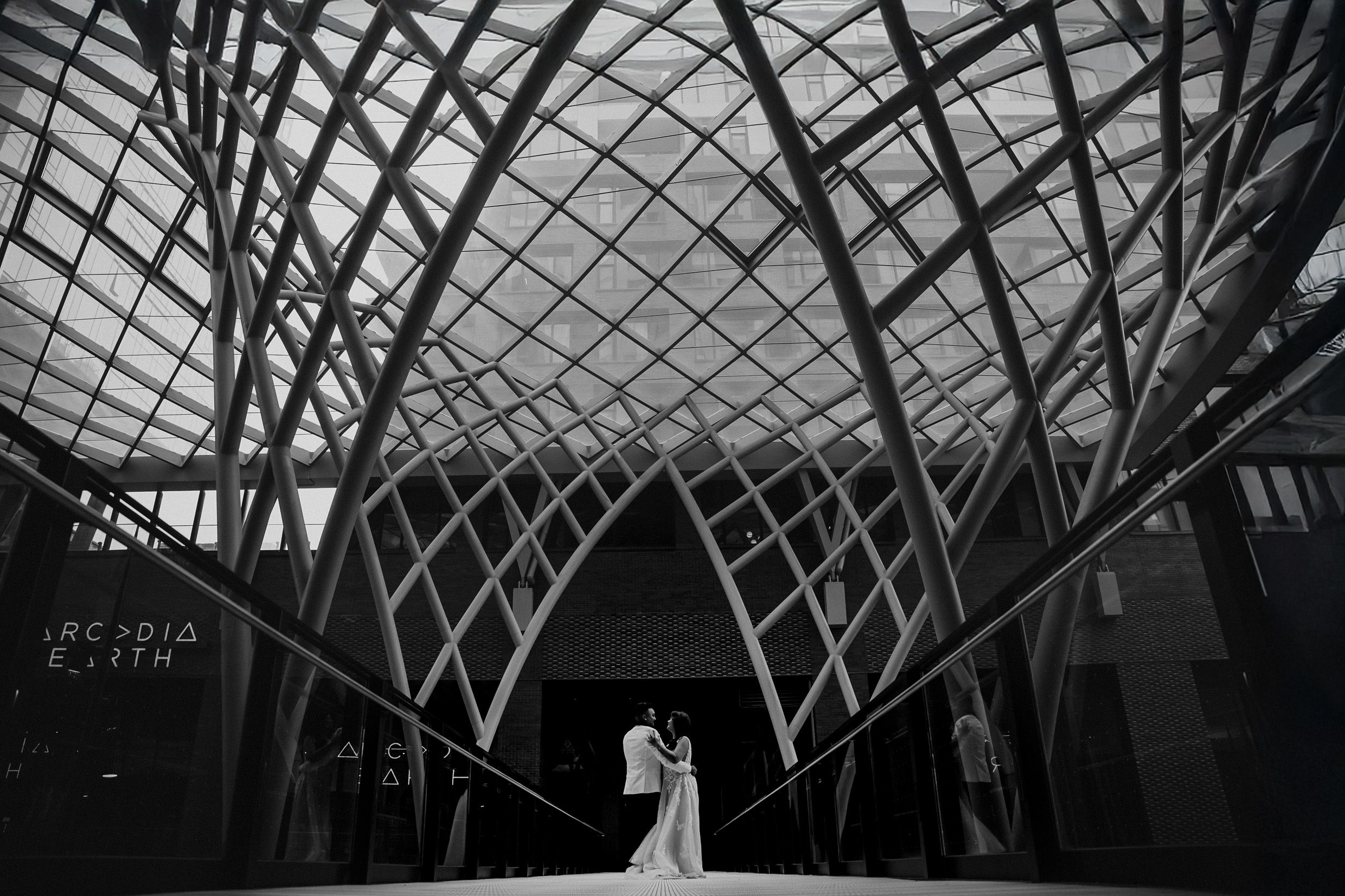 Black and white photo of architectural lattice structure framing figures in the center.