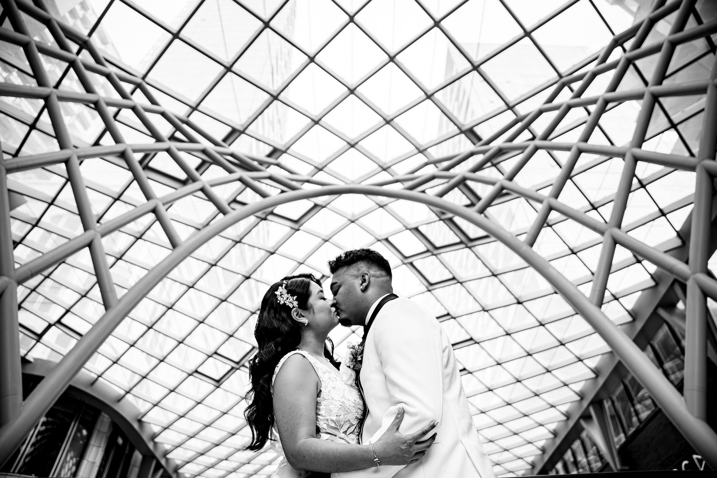 A romantic moment captured under a geometric glass ceiling with dramatic black and white lighting.