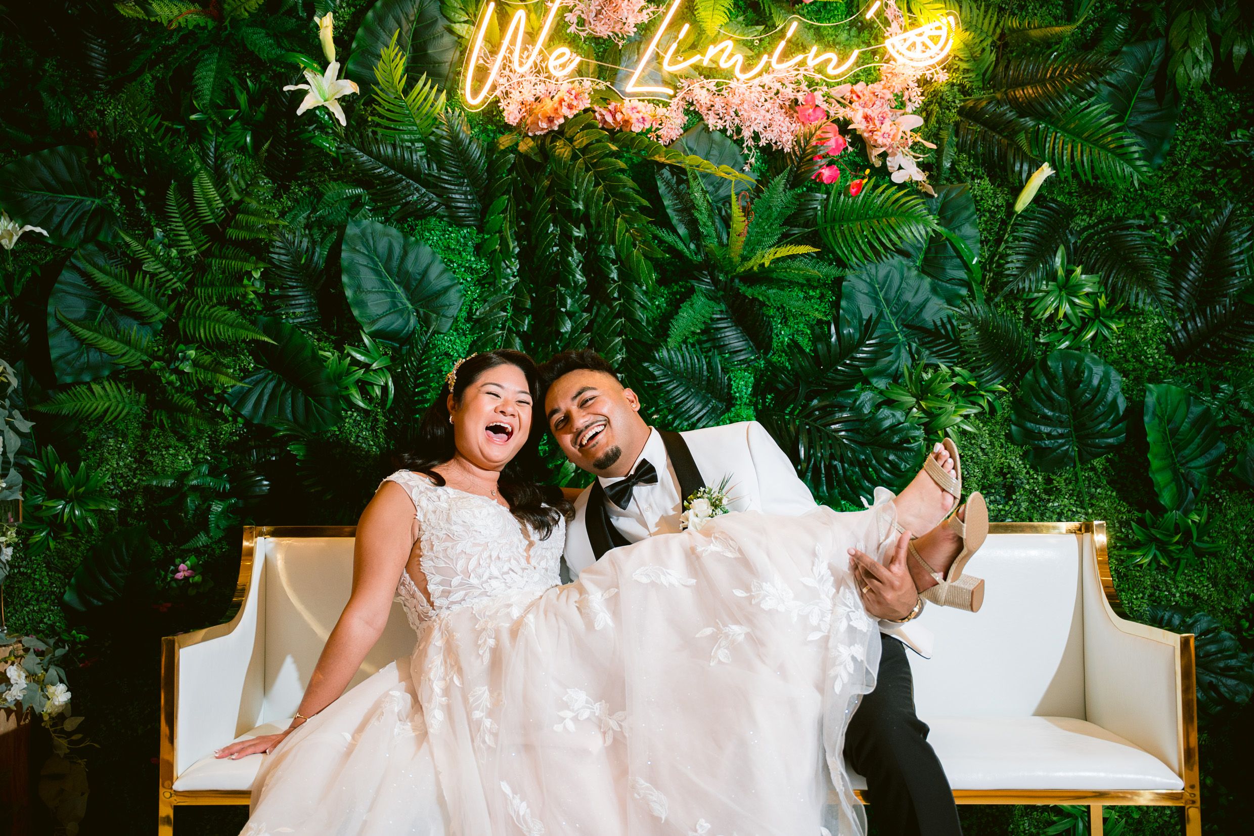 Two people sharing a joyful laugh while seated on white furniture surrounded by lush tropical decor.