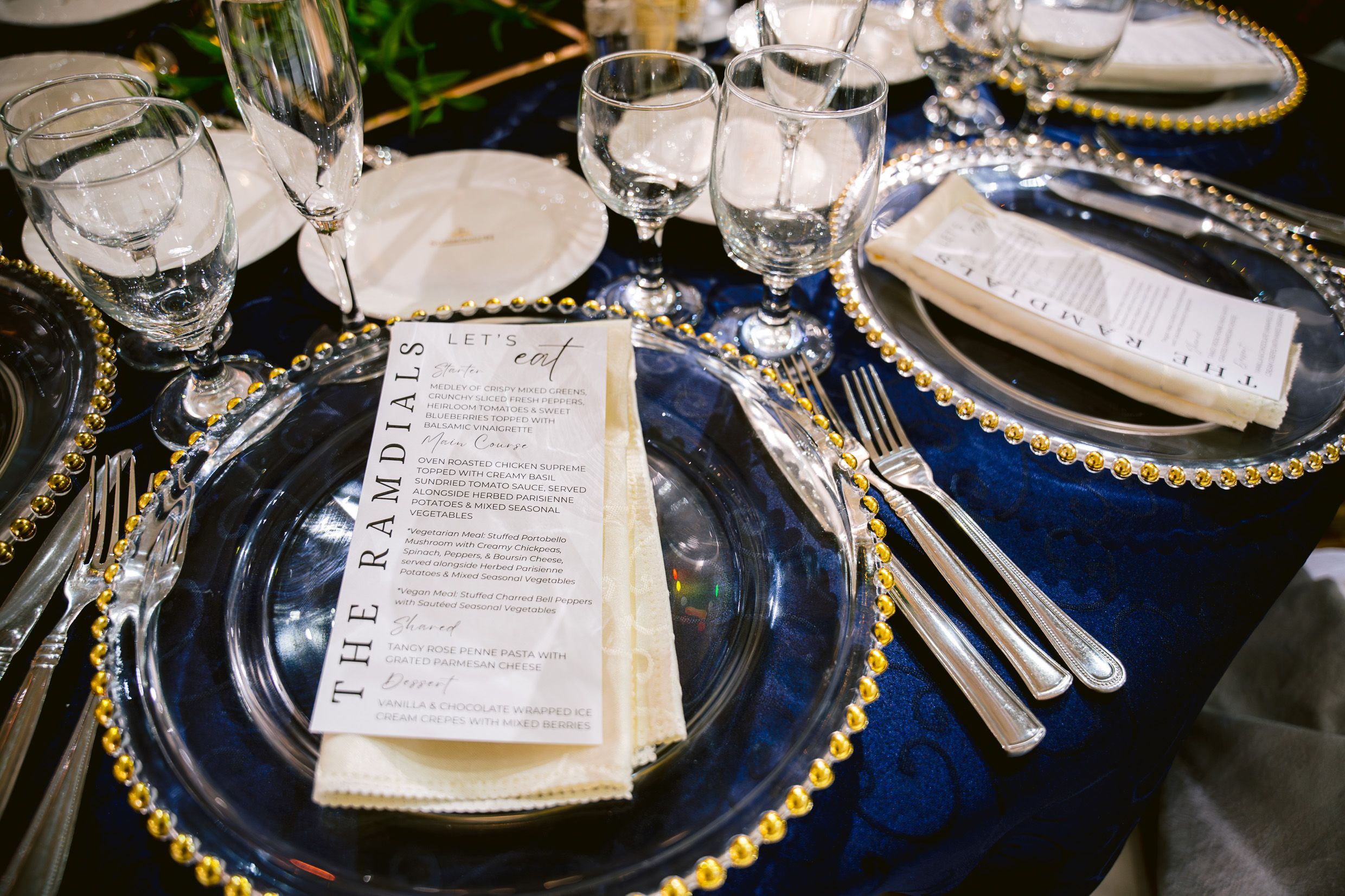 An elegant wedding table setting features navy chargers, gold accents, and printed menus.