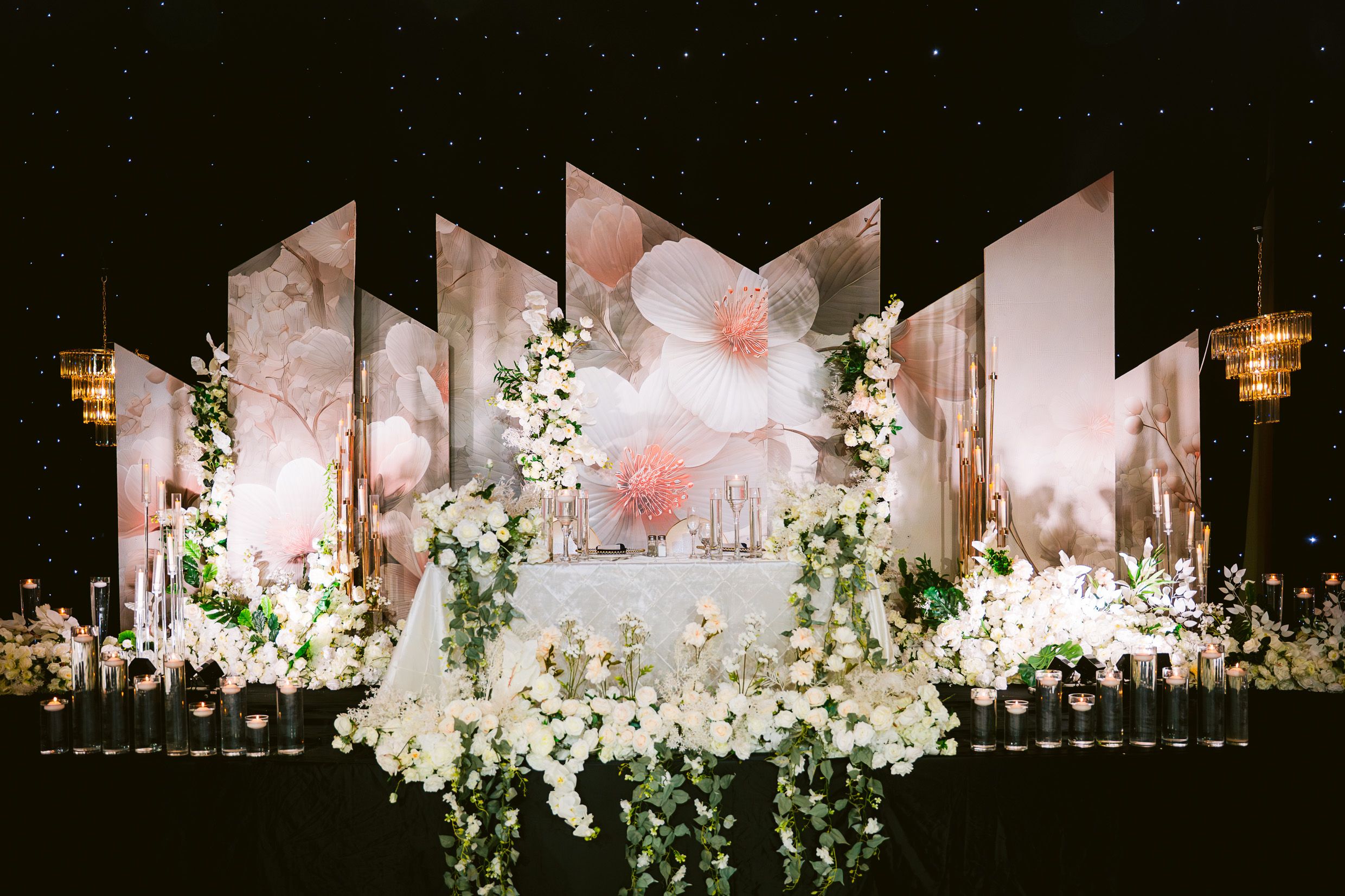 Modern wedding reception stage with geometric panels and cascading white floral arrangements.