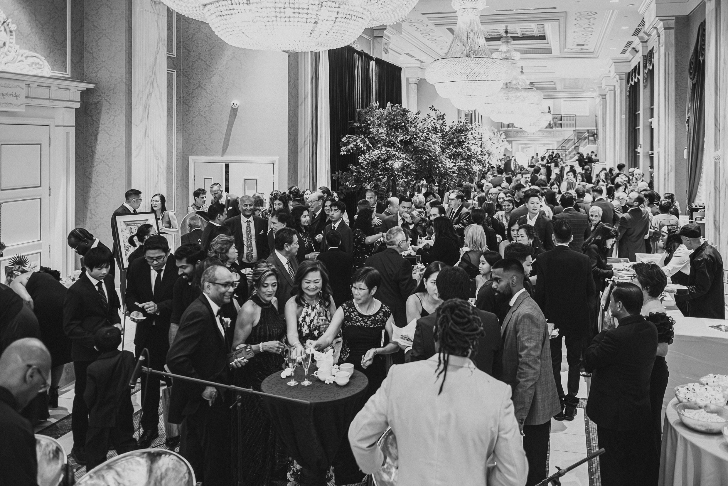Vintage black and white photo of elegant reception crowd mingling in grand hallway.