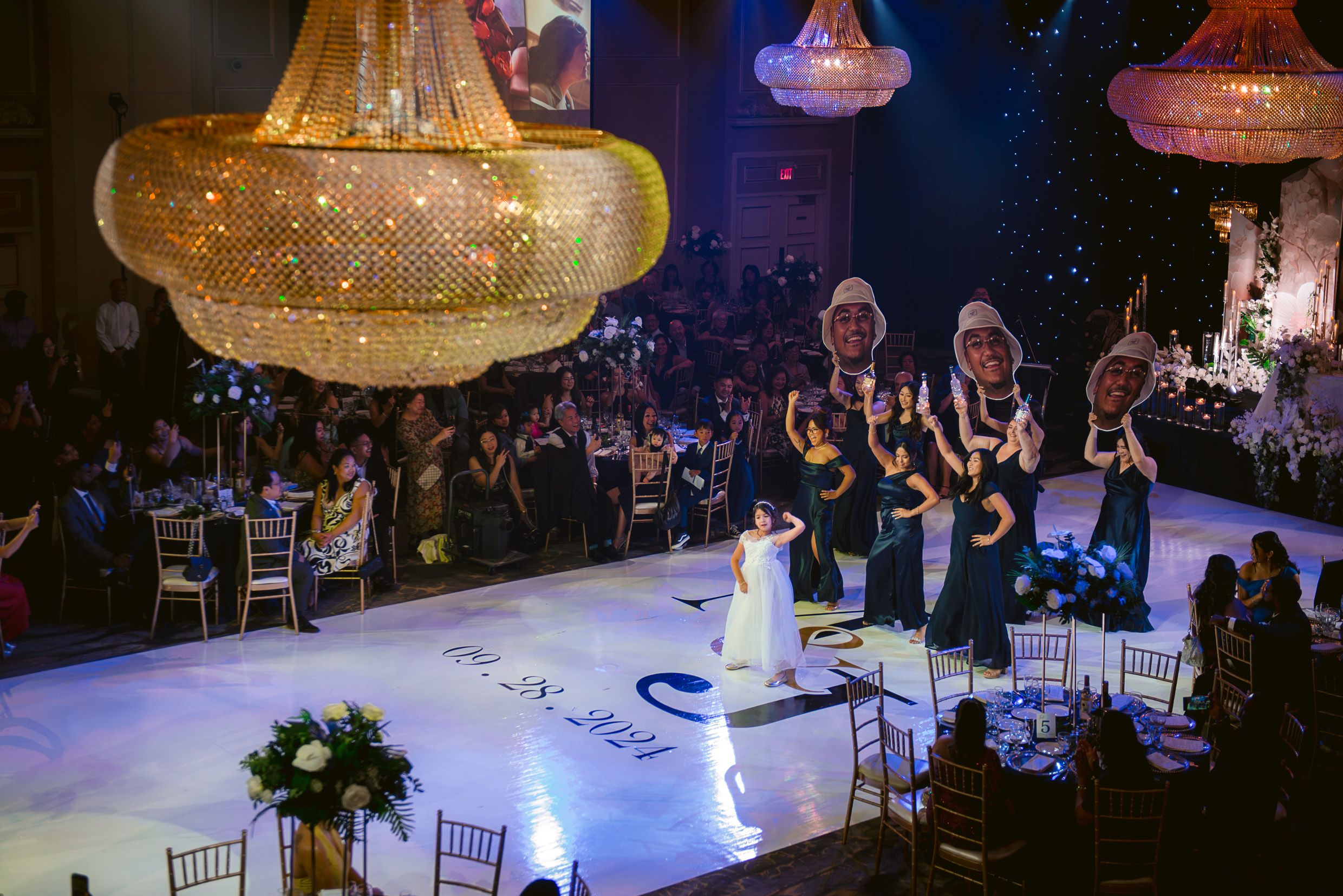 A grand ballroom with golden chandeliers hosts an elegant wedding first dance.