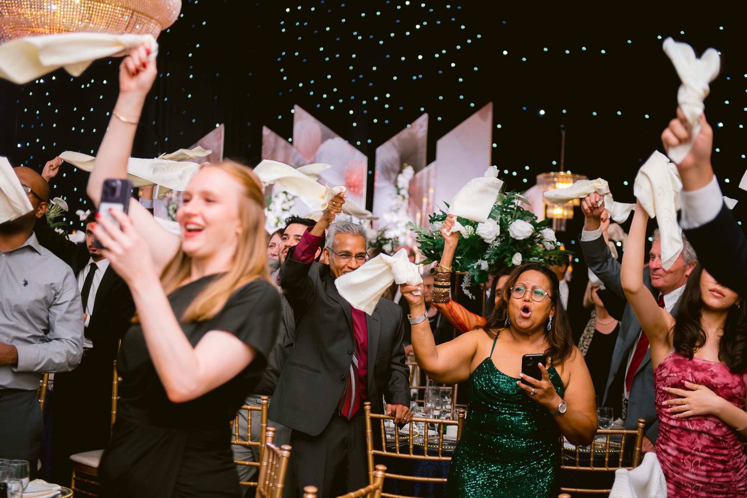 Joyful wedding party guests dancing and celebrating with confetti in the air during an evening reception.