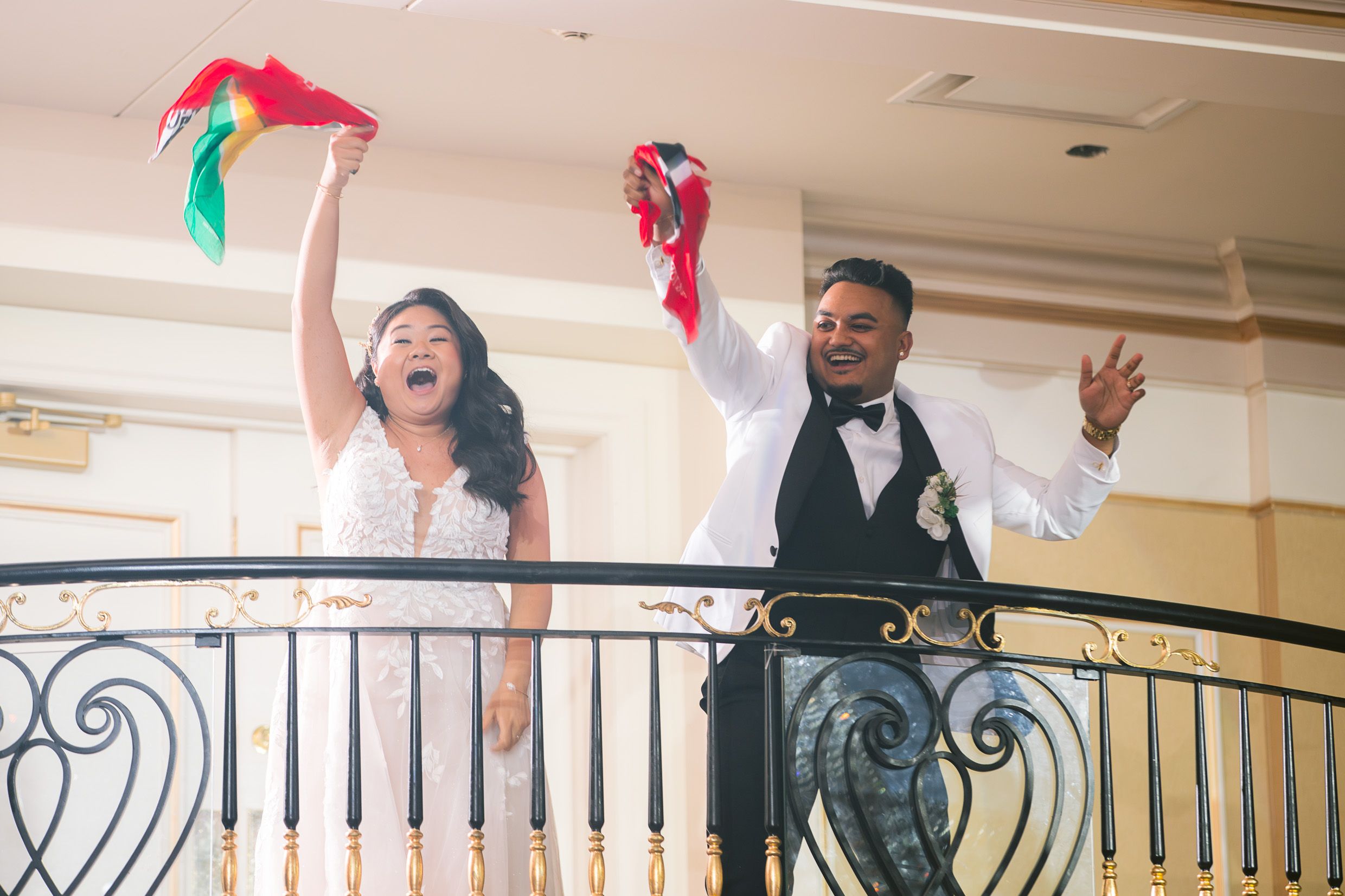 Joyful couple celebrating on an ornate balcony with decorative fabric streamers and formal attire.