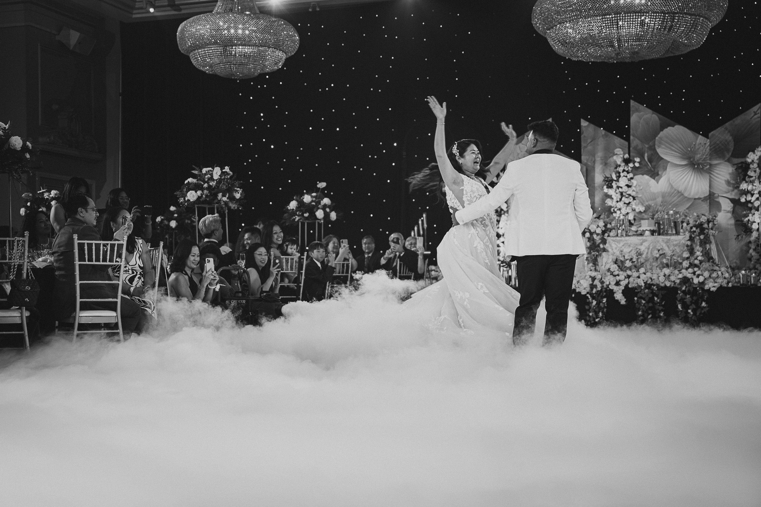 A couple dancing on a fog-covered dance floor during a wedding reception with hanging lights overhead.