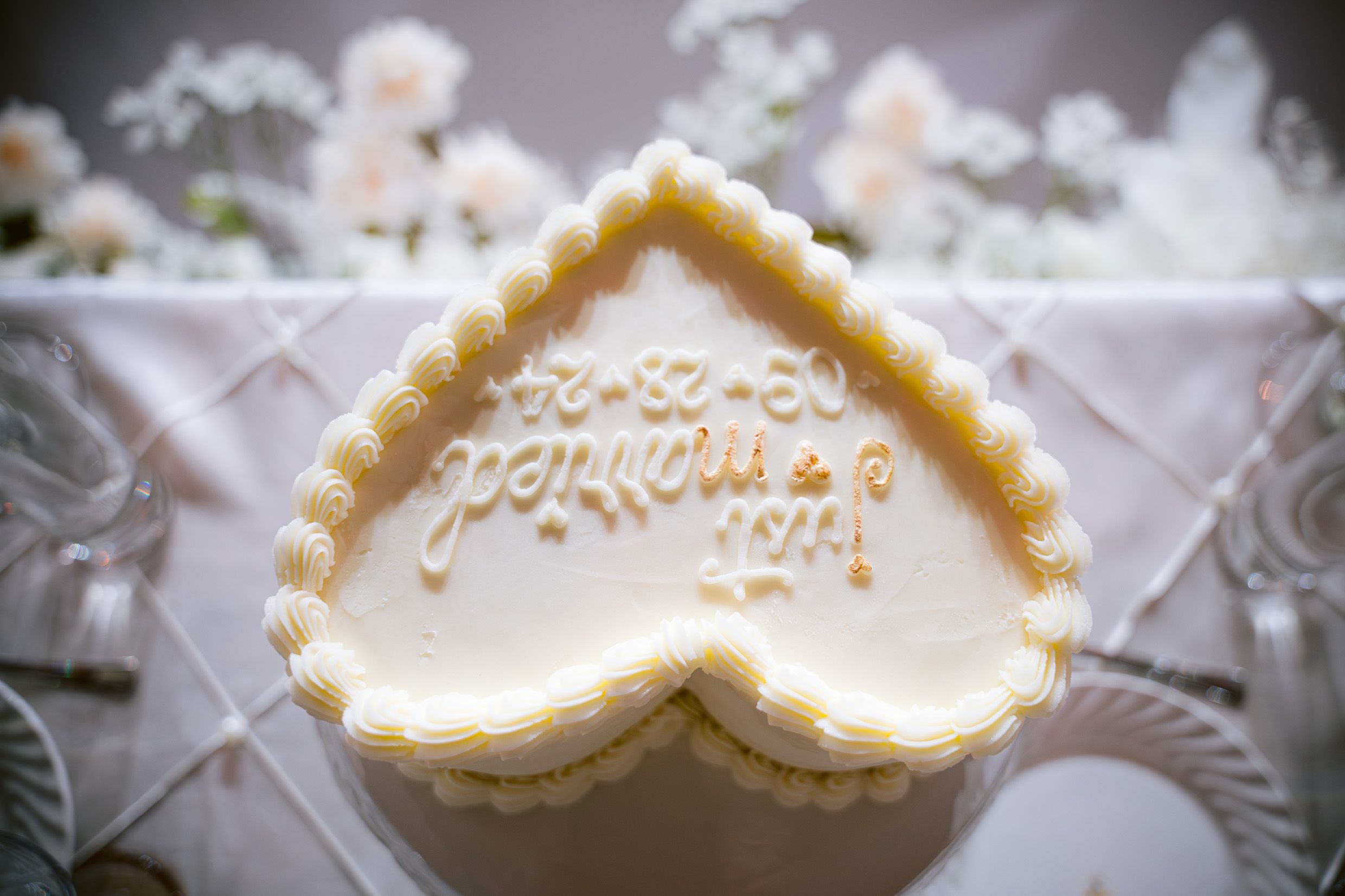 A heart-shaped white wedding cake design with delicate icing detail captures an intimate decorative moment.