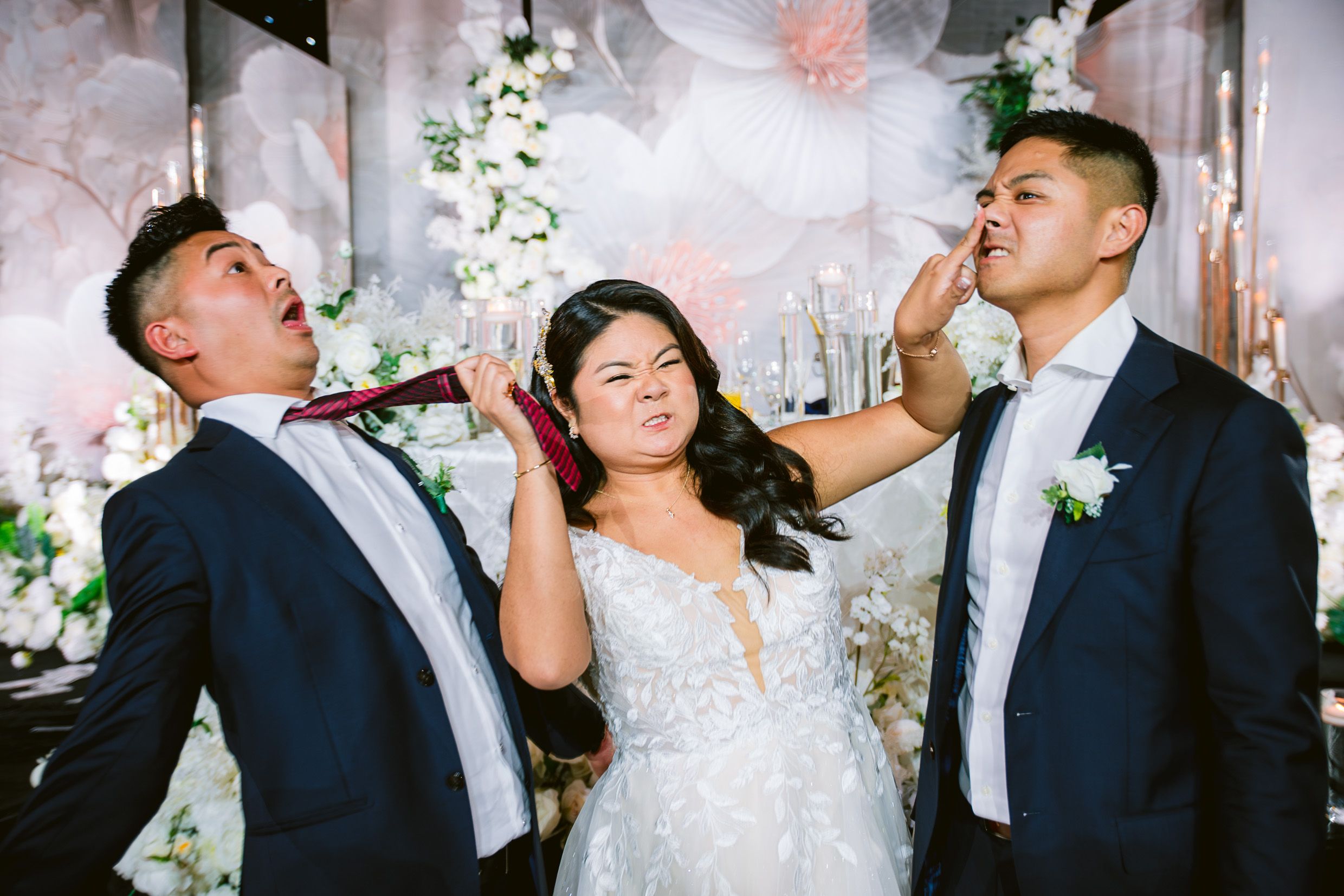 Wedding party participants joyfully blowing bubbles together during celebration with floral decorations in background.
