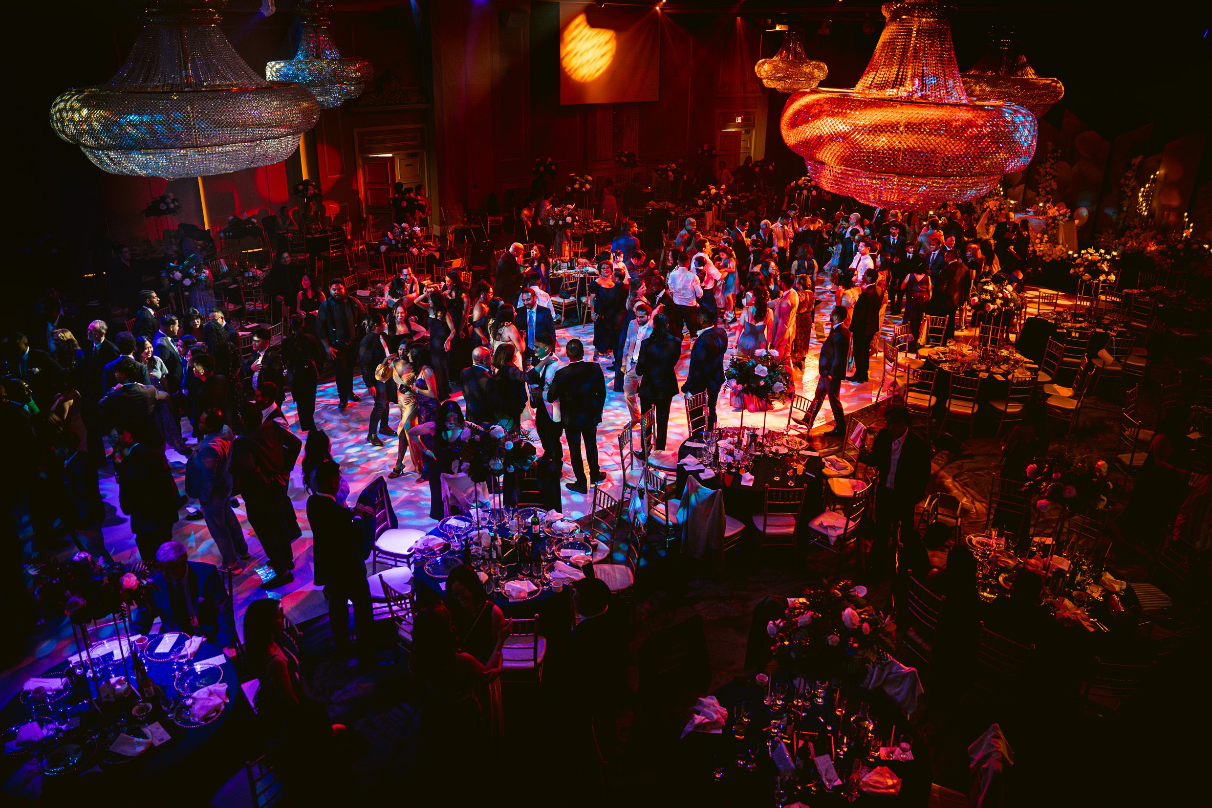 Overhead view of a dimly lit event space with purple and red lighting illuminating a crowd gathered on the dance floor.