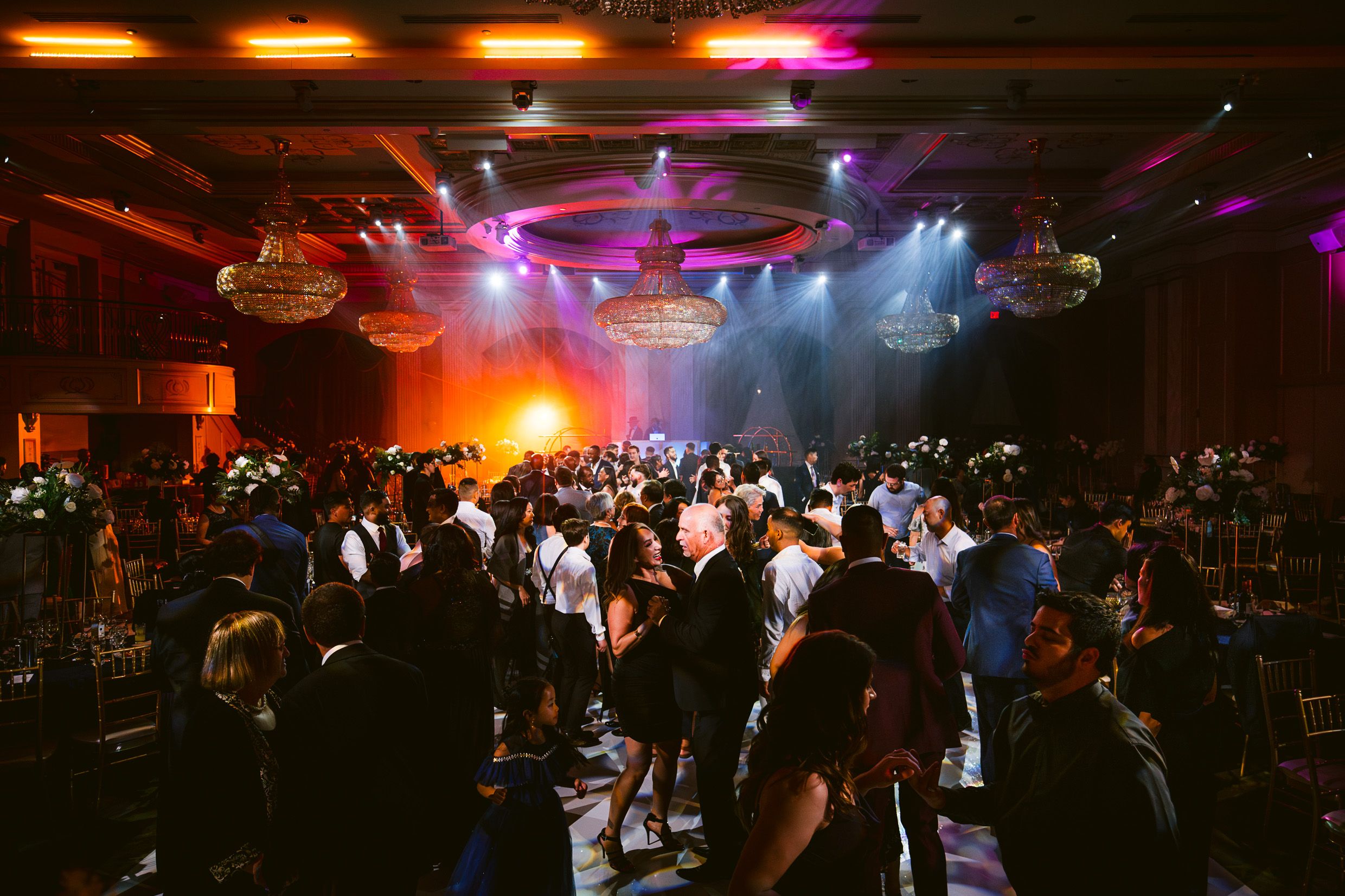 A crowded nightclub dance floor with colorful lighting and disco balls creating an energetic party atmosphere.