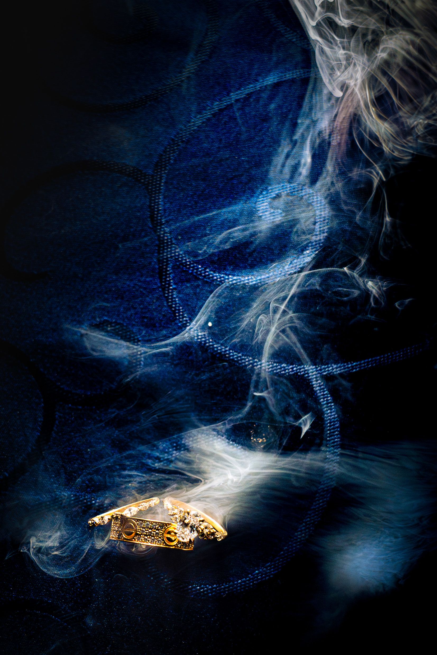 Dramatic artistic photo of burning cigarette emitting swirling smoke patterns against dark blue background.