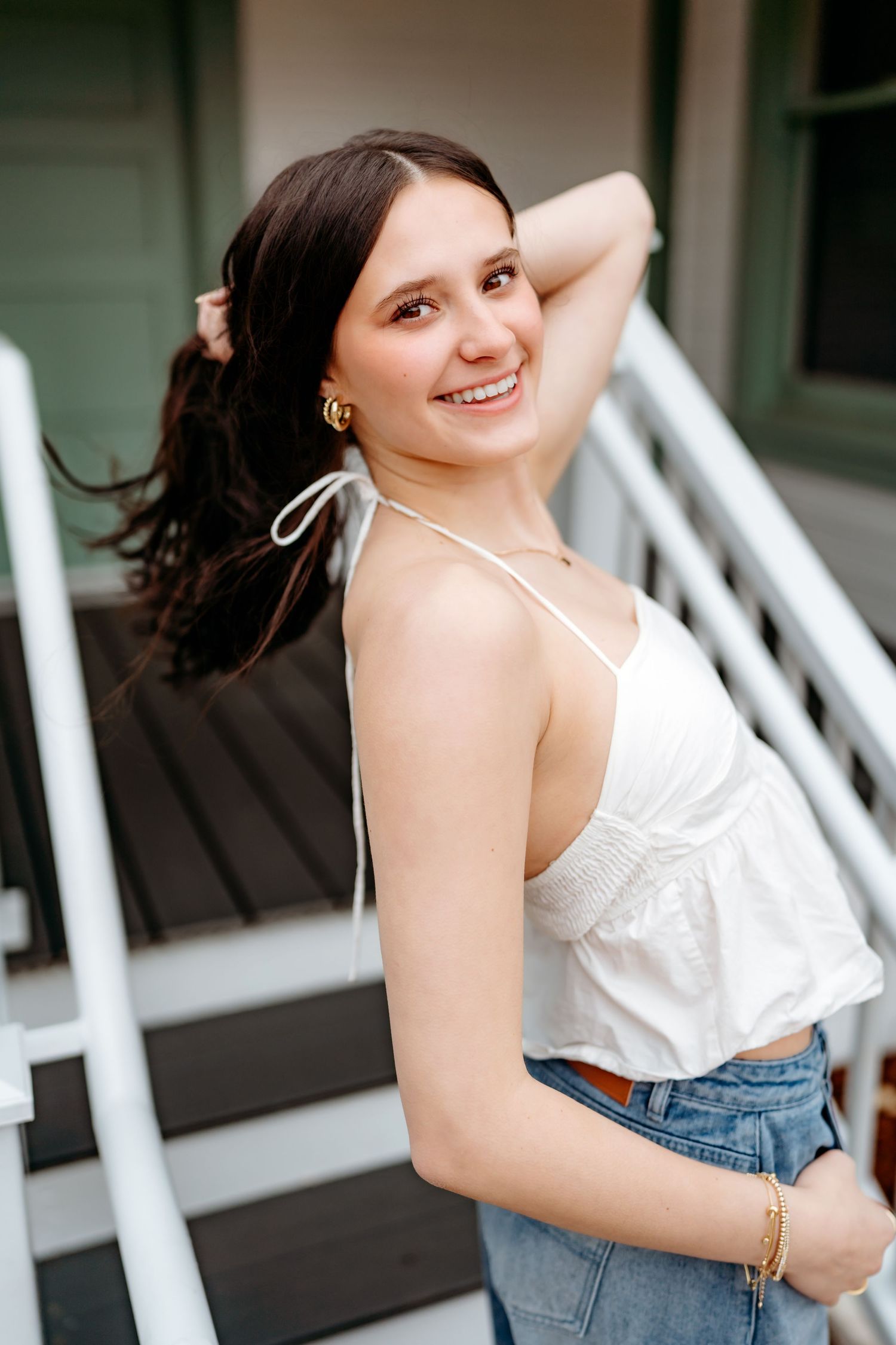 A person in a white summer top and jeans poses on stairs with a warm smile.