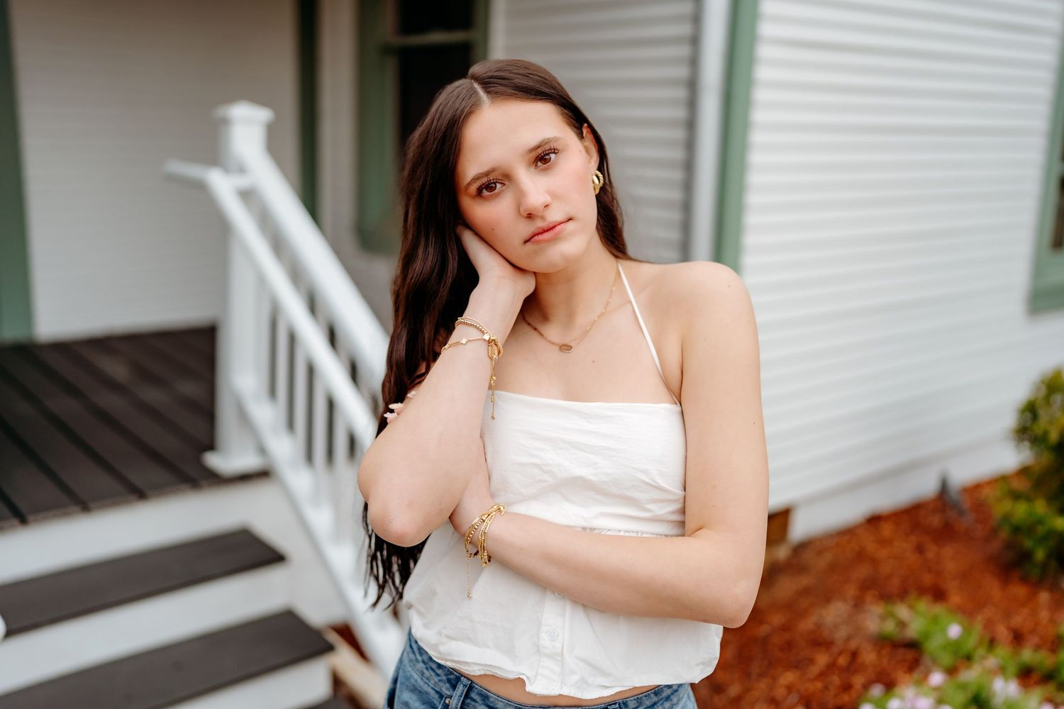 Someone in a white crop top and jeans stands casually on a porch by a white railing.