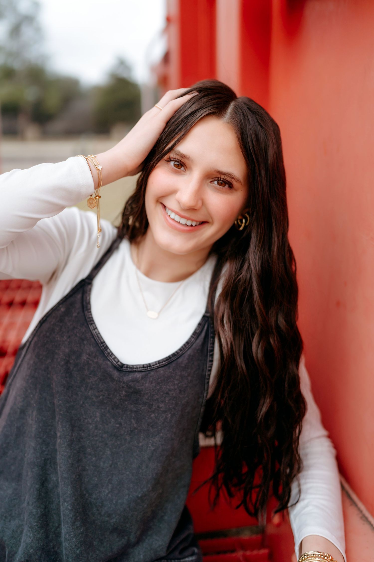 Woman with long dark hair wearing a white shirt and dark vest smiles warmly against a bright red wall.