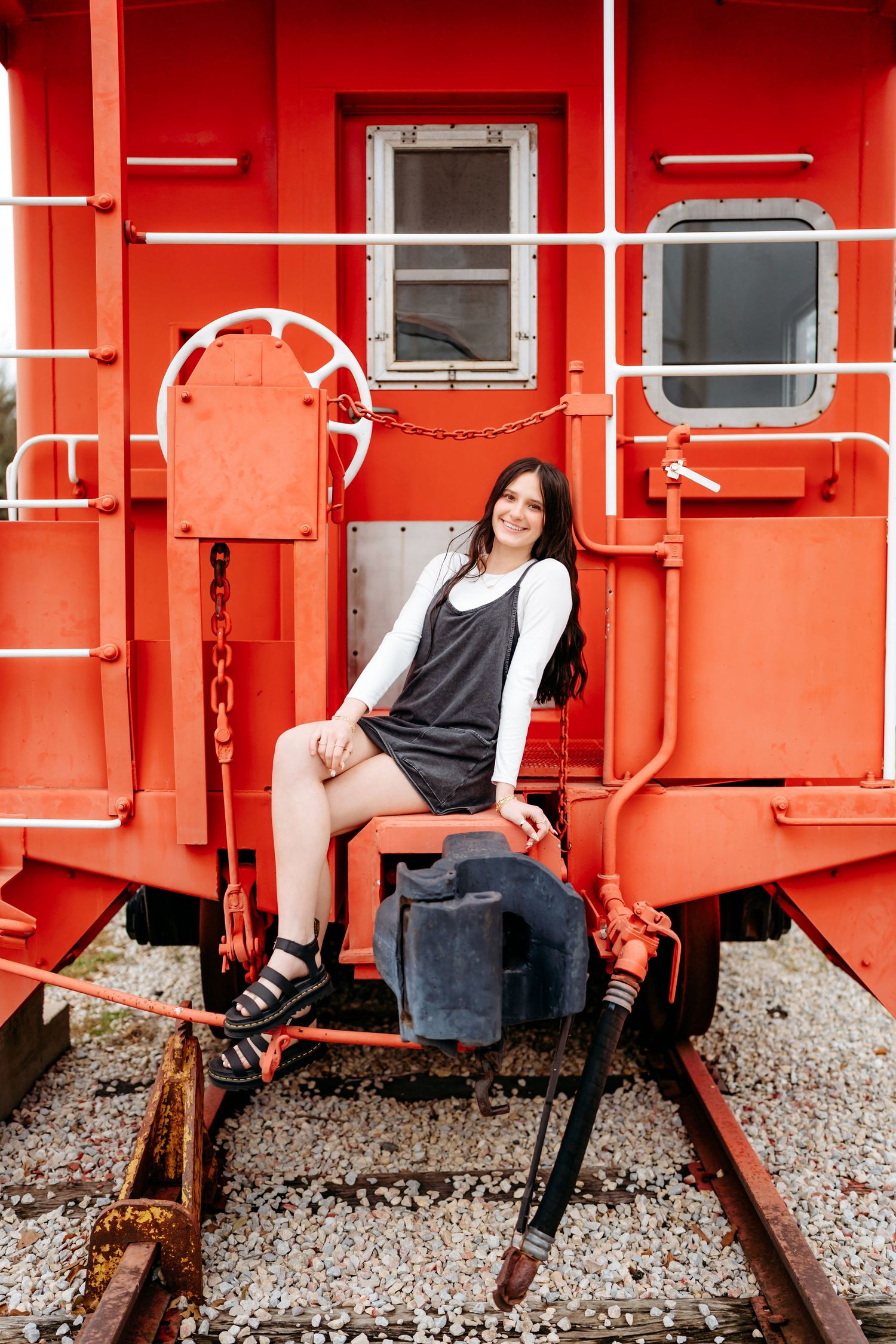 A person poses on the back of a vibrant red vintage train caboose on a railroad track.