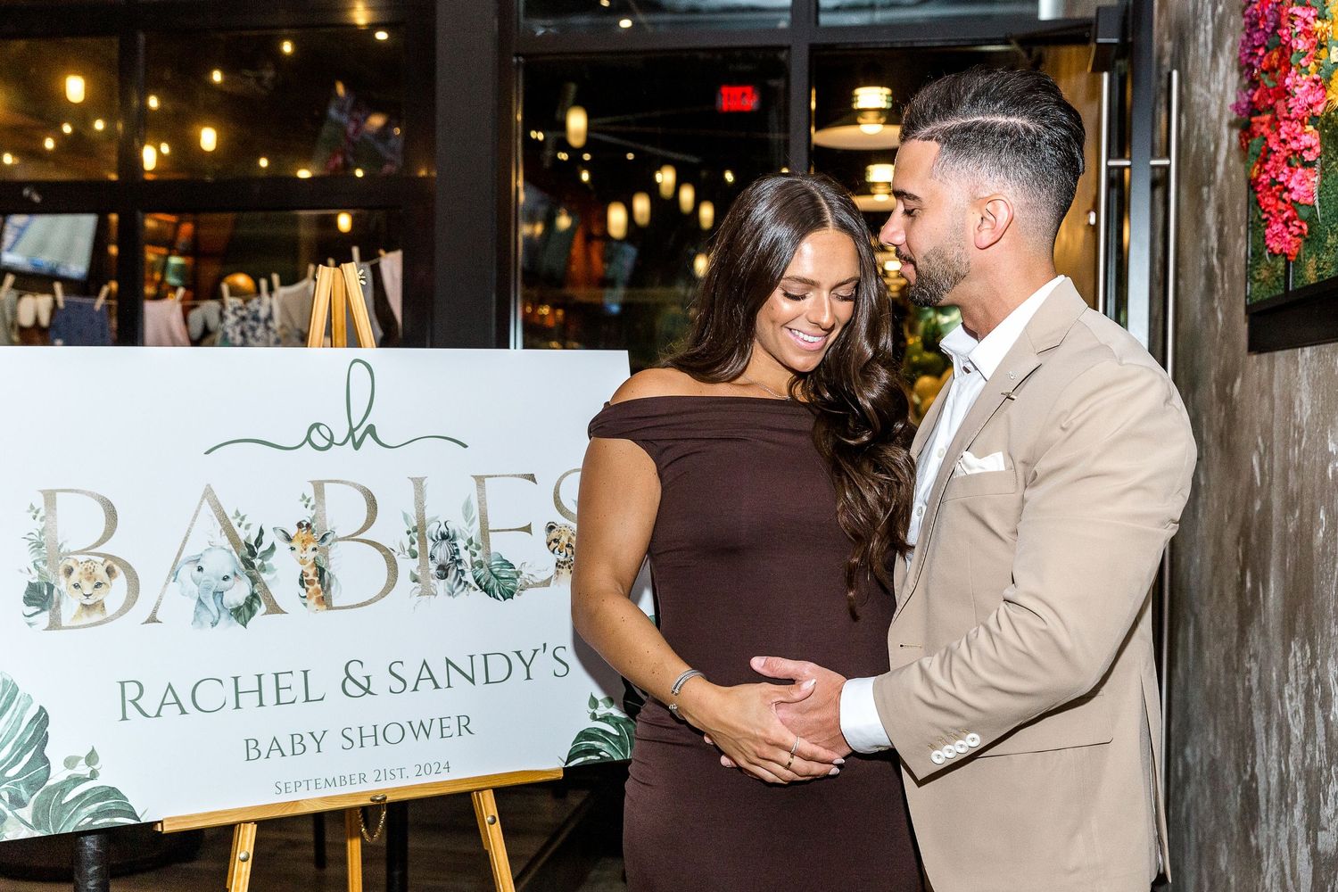 Baby shower welcome sign with elegant design and string lights in background.