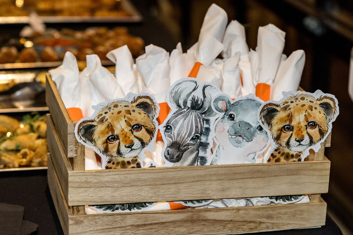 Wooden box filled with safari animal themed party favors and white napkins.
