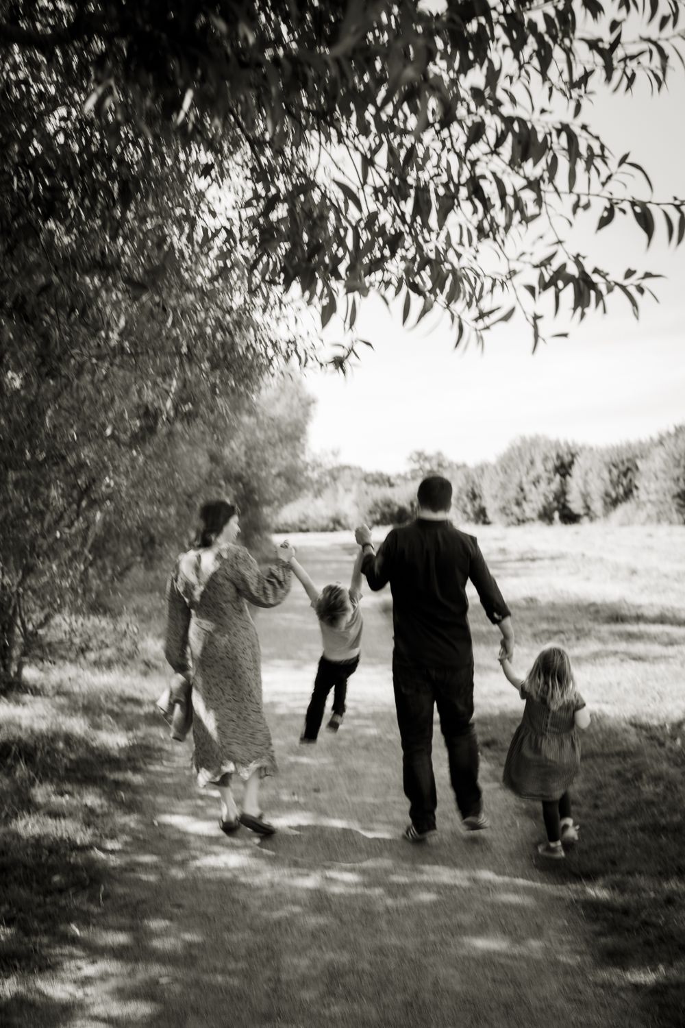 Black and white image showing the back of a family. They are all holding hands and the mum and dad are swinging their son.