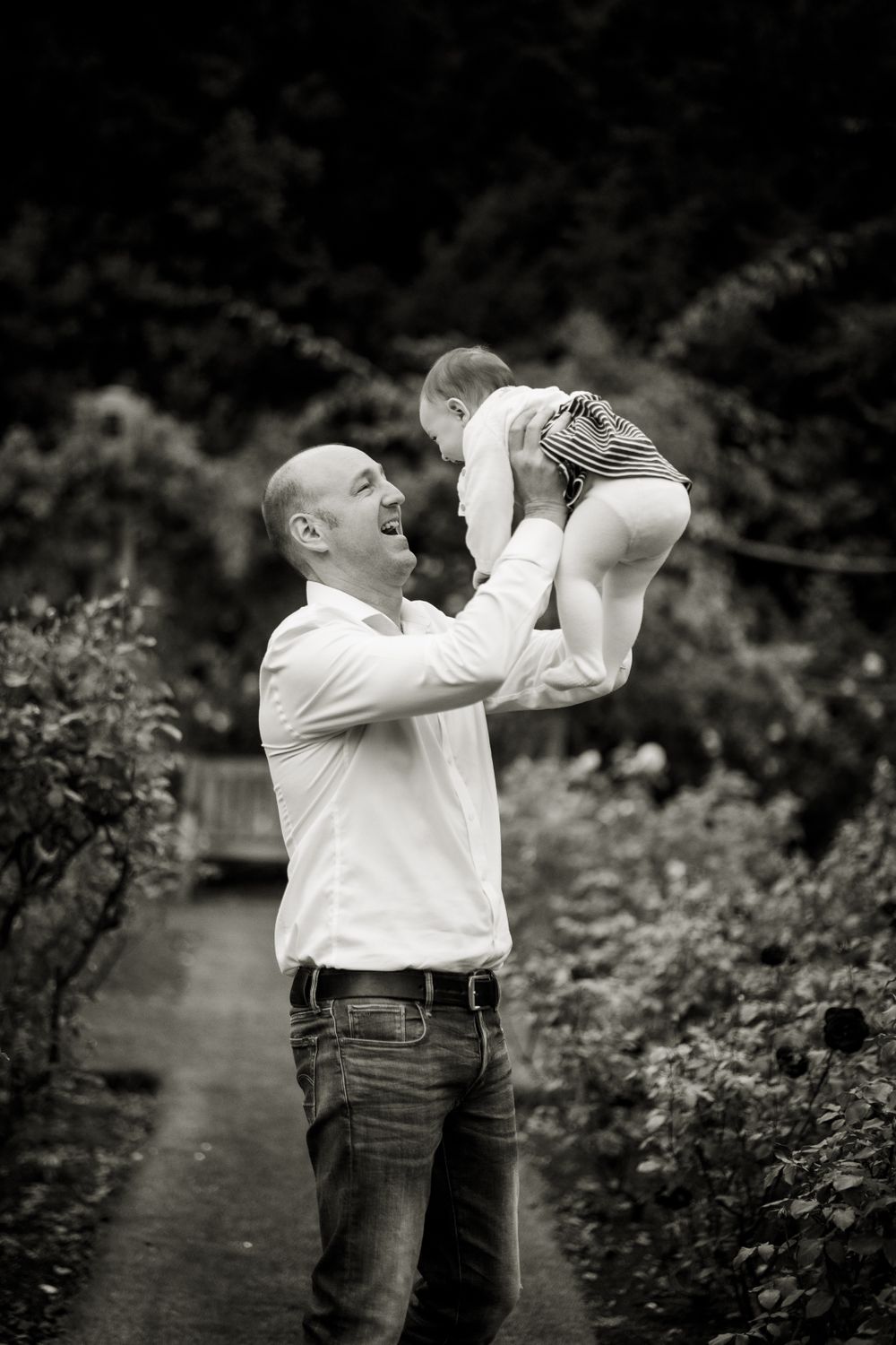 Dad playing with his baby girl and lifting her up over his head in Regents park, for a family photoshoot with Jane Nicholson Photography.