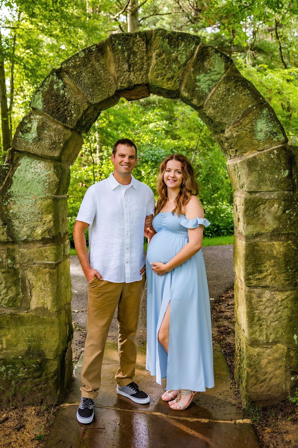 A couple poses playfully together among stone archways surrounded by vibrant greenery.