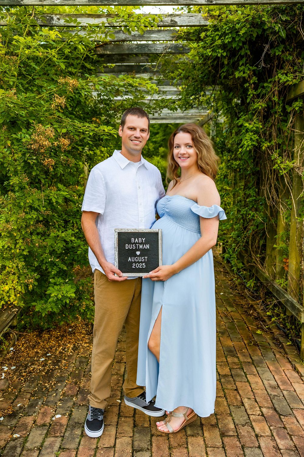 Pregnancy announcement photoshoot in a garden setting with a couple holding a letter board.