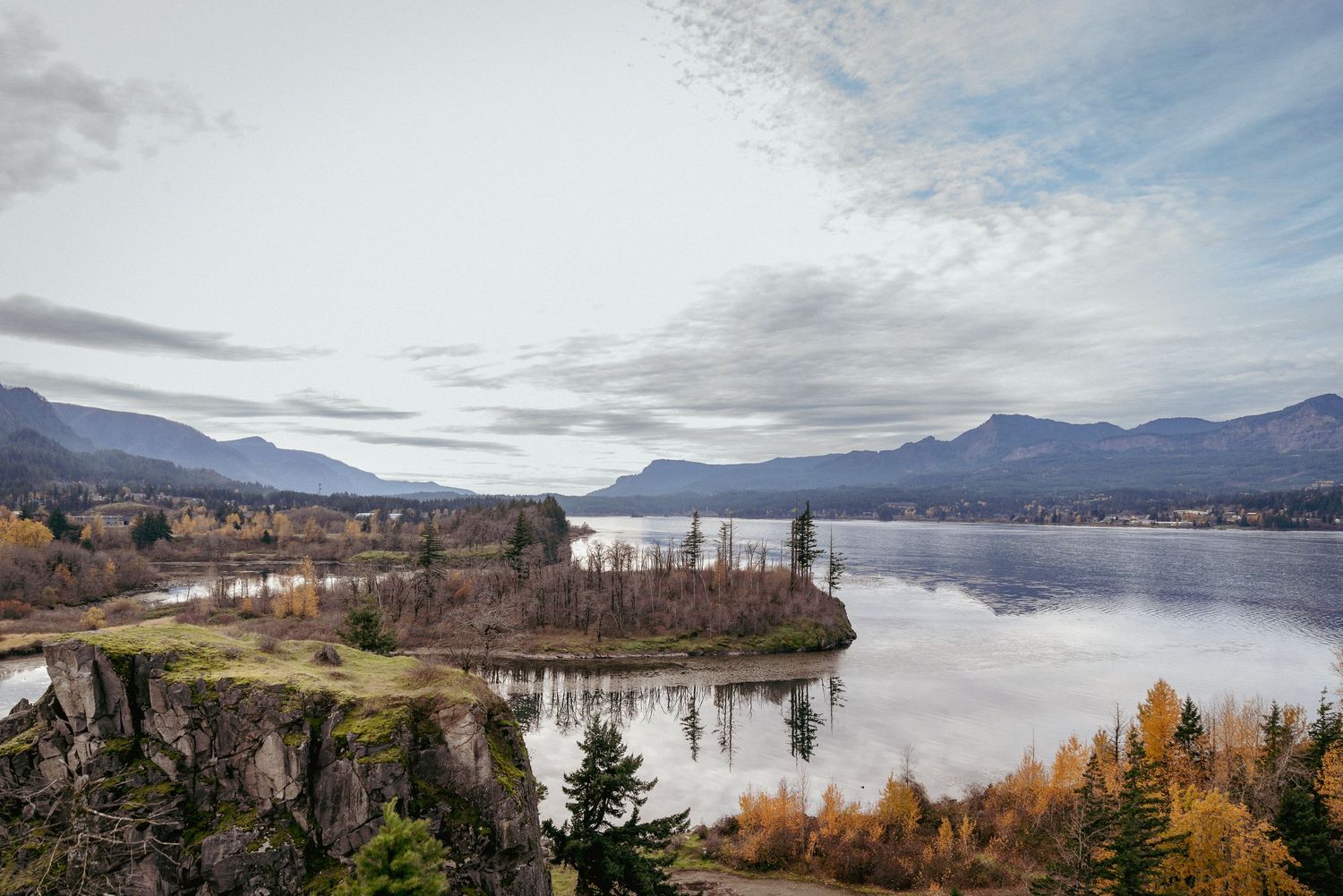 Aerial view of Columbia River with vibrant autumn forest and mountain range in the background during fall season.